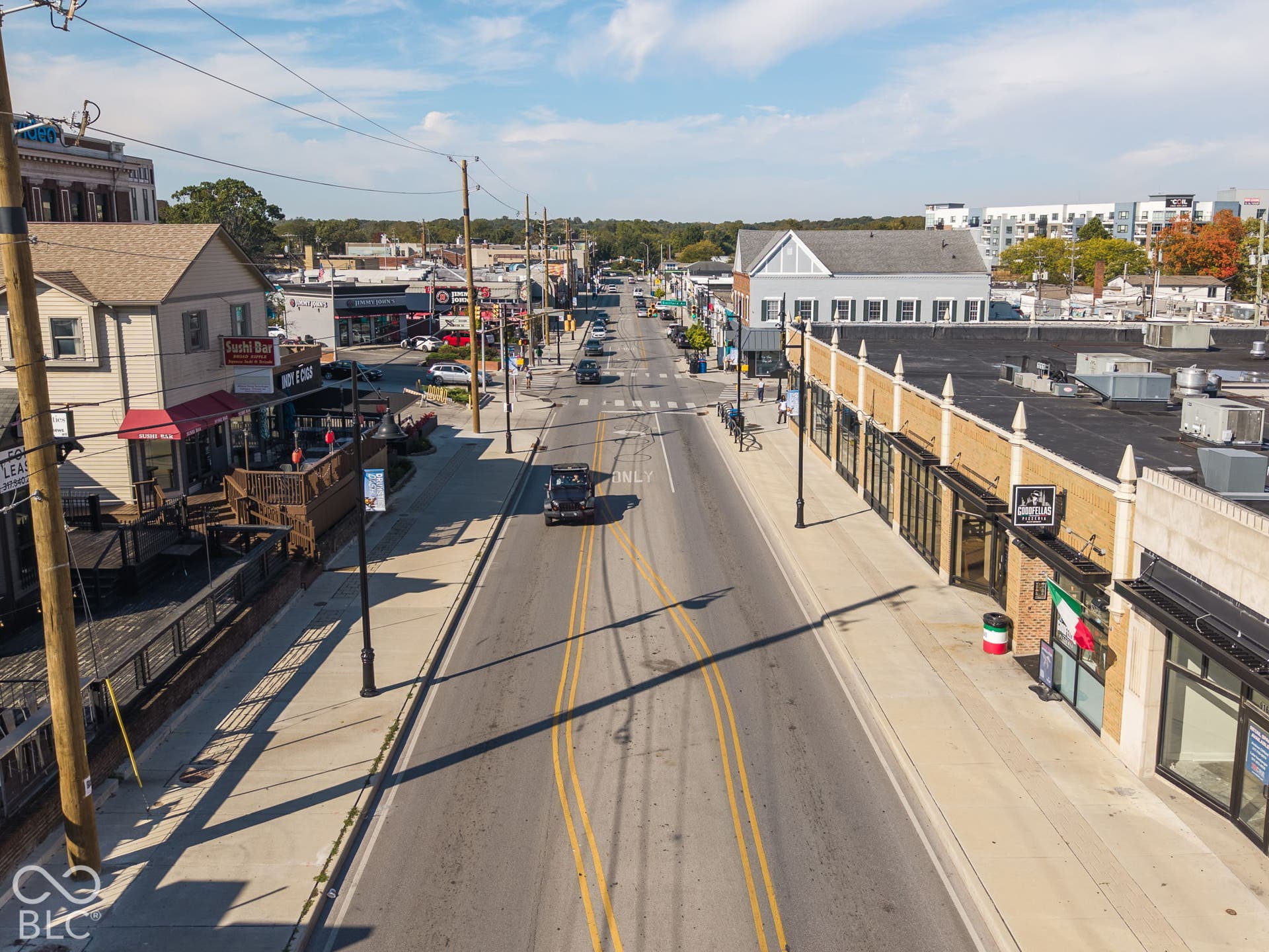 Aerial perspective of a streetscape featuring mixed-use commercial buildings, sidewalk accessibility, utility infrastructure, paved thoroughfare, and varied architectural styles