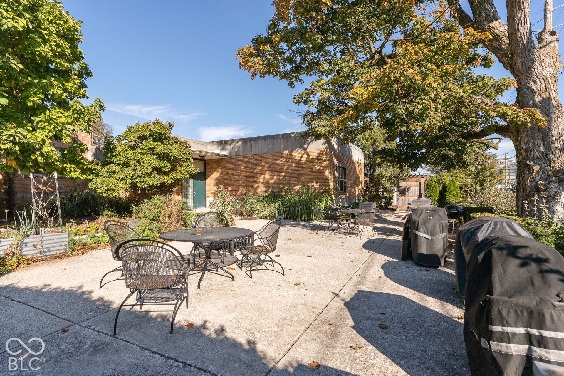 Concrete patio featuring brick exterior wall construction, mature trees, and perimeter garden beds
