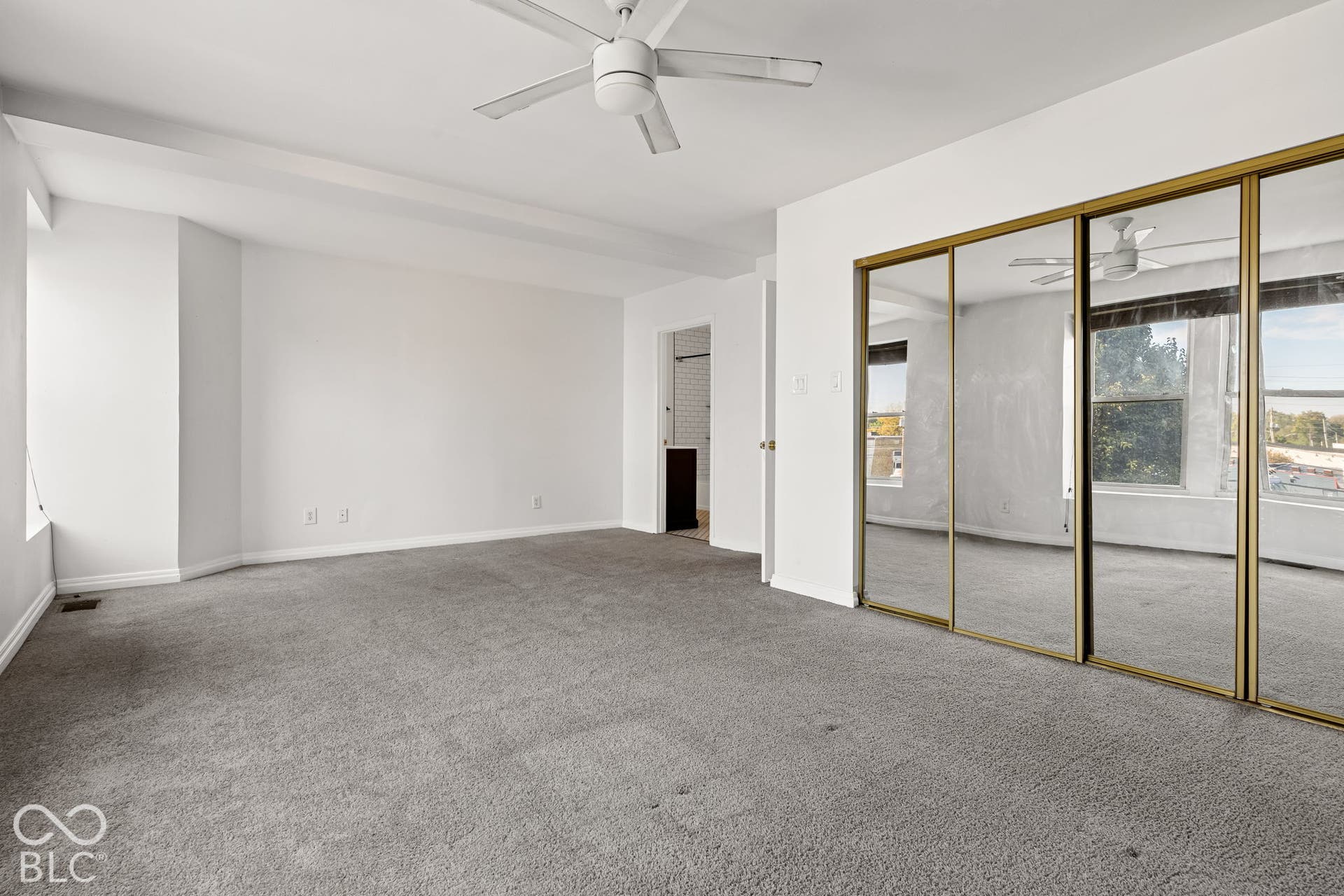 Interior space featuring wall-to-wall carpeting, floor-to-ceiling mirrored sliding closet doors with gold-tone frames, and a white ceiling fan with integrated lighting