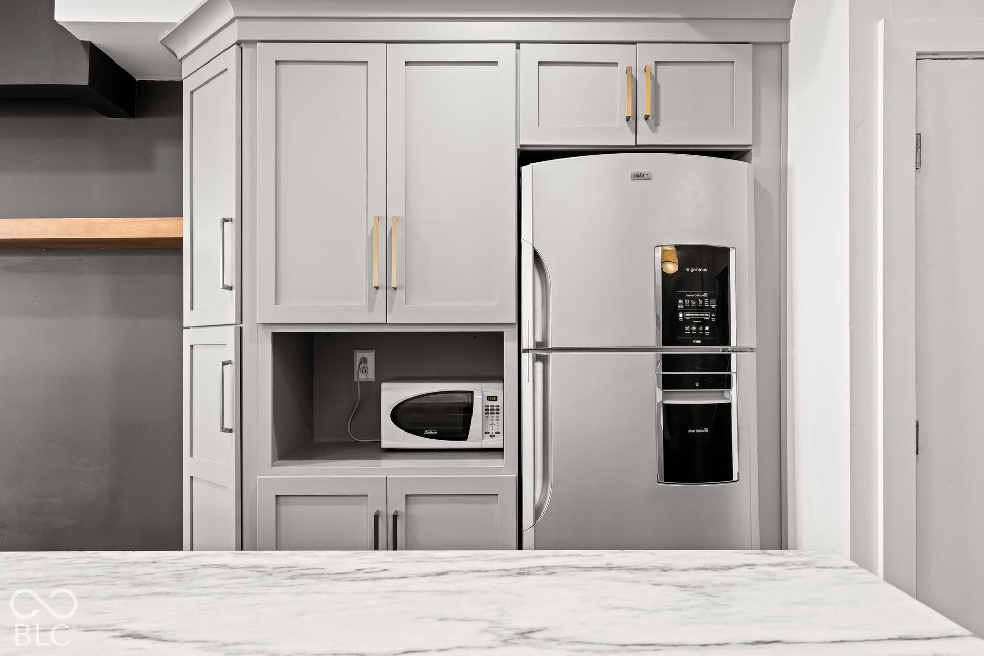 Custom cabinetry featuring matte gray finish and gold-tone hardware, stone-surface countertop, and stainless steel refrigerator