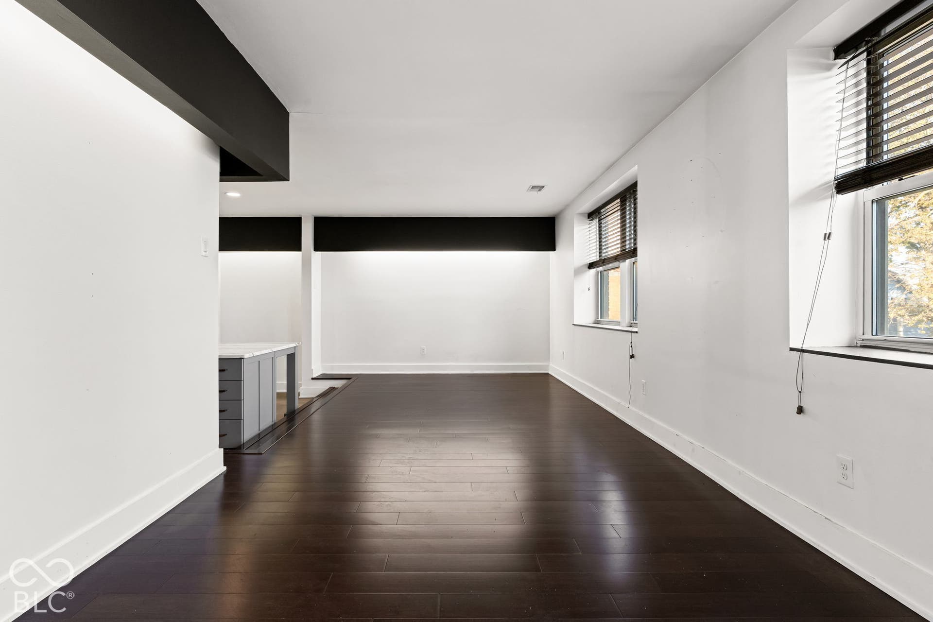 Interior space featuring dark wood-finish flooring, high-contrast black architectural ceiling accents, recessed lighting, and multiple windows with integrated blinds