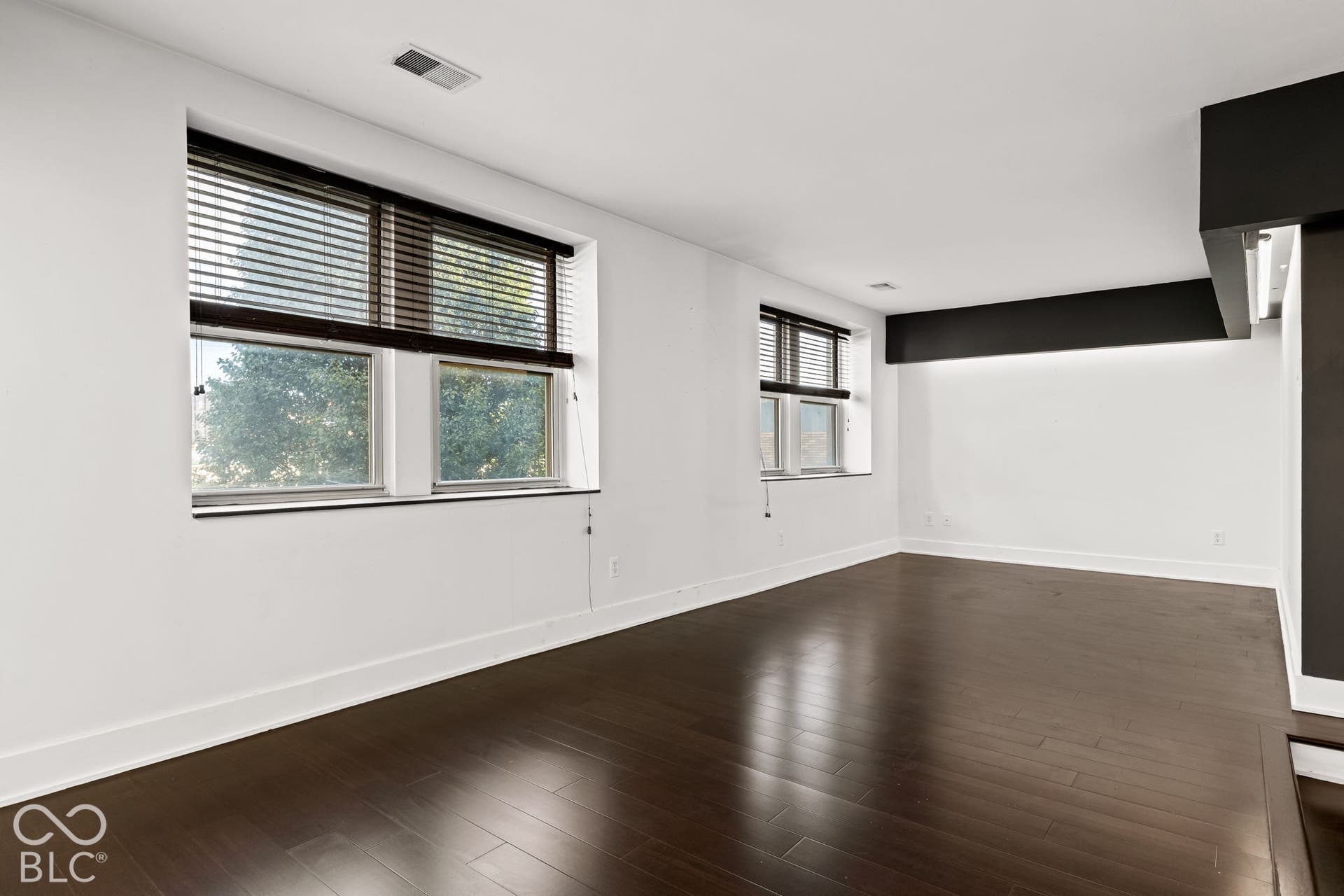 Room featuring wood-finish flooring, dual windows with horizontal blinds, and recessed lighting