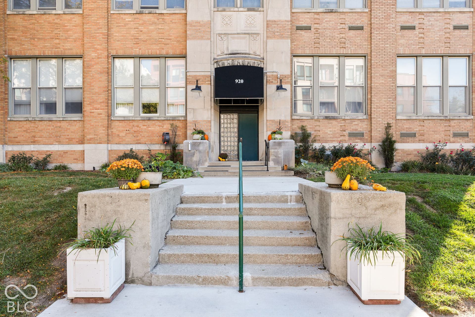 Brick building exterior featuring stone detailing, multi-pane windows, a recessed entryway, and concrete stairs with metal railings