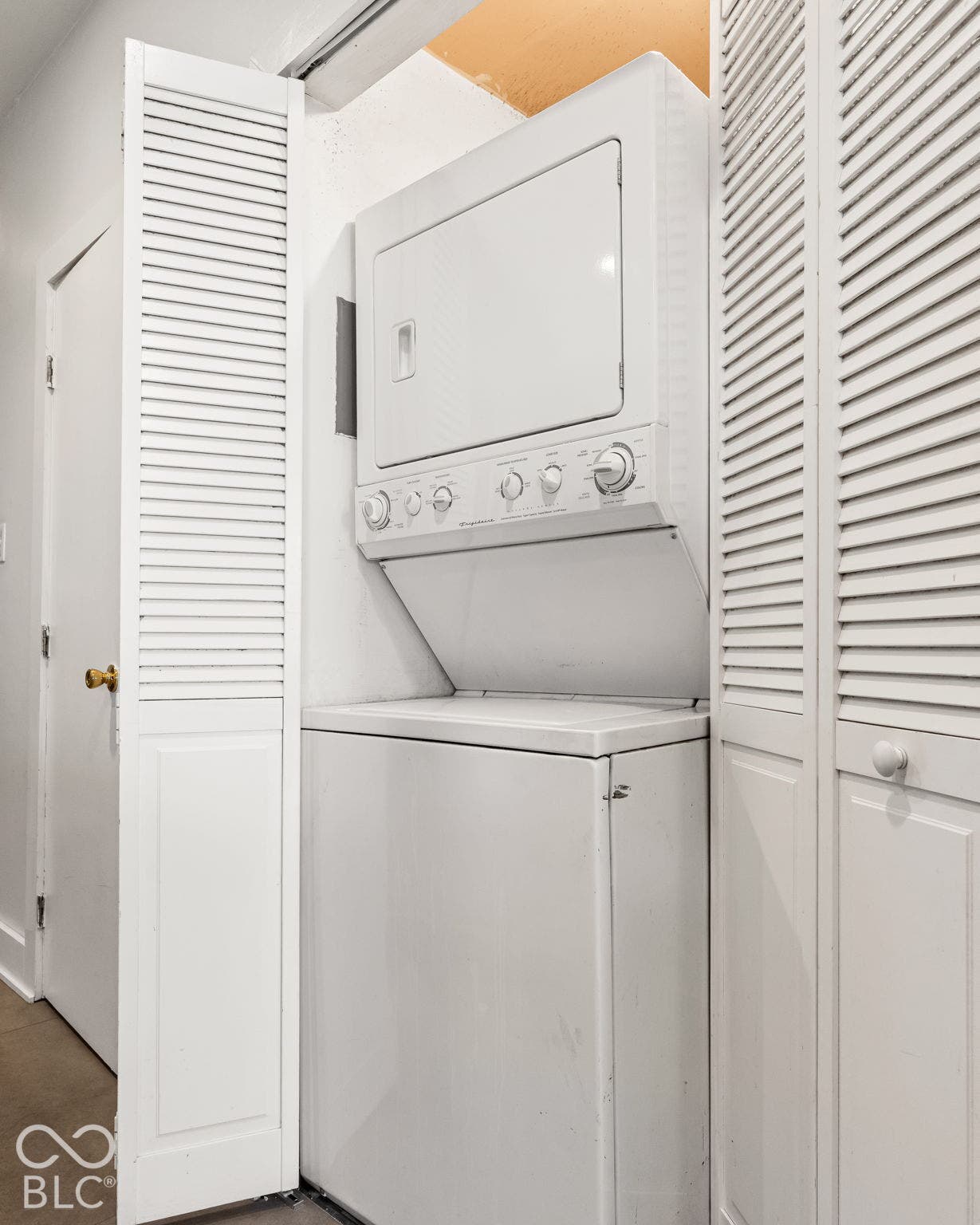 Stacked white washer and dryer unit enclosed by bi-fold louvered doors