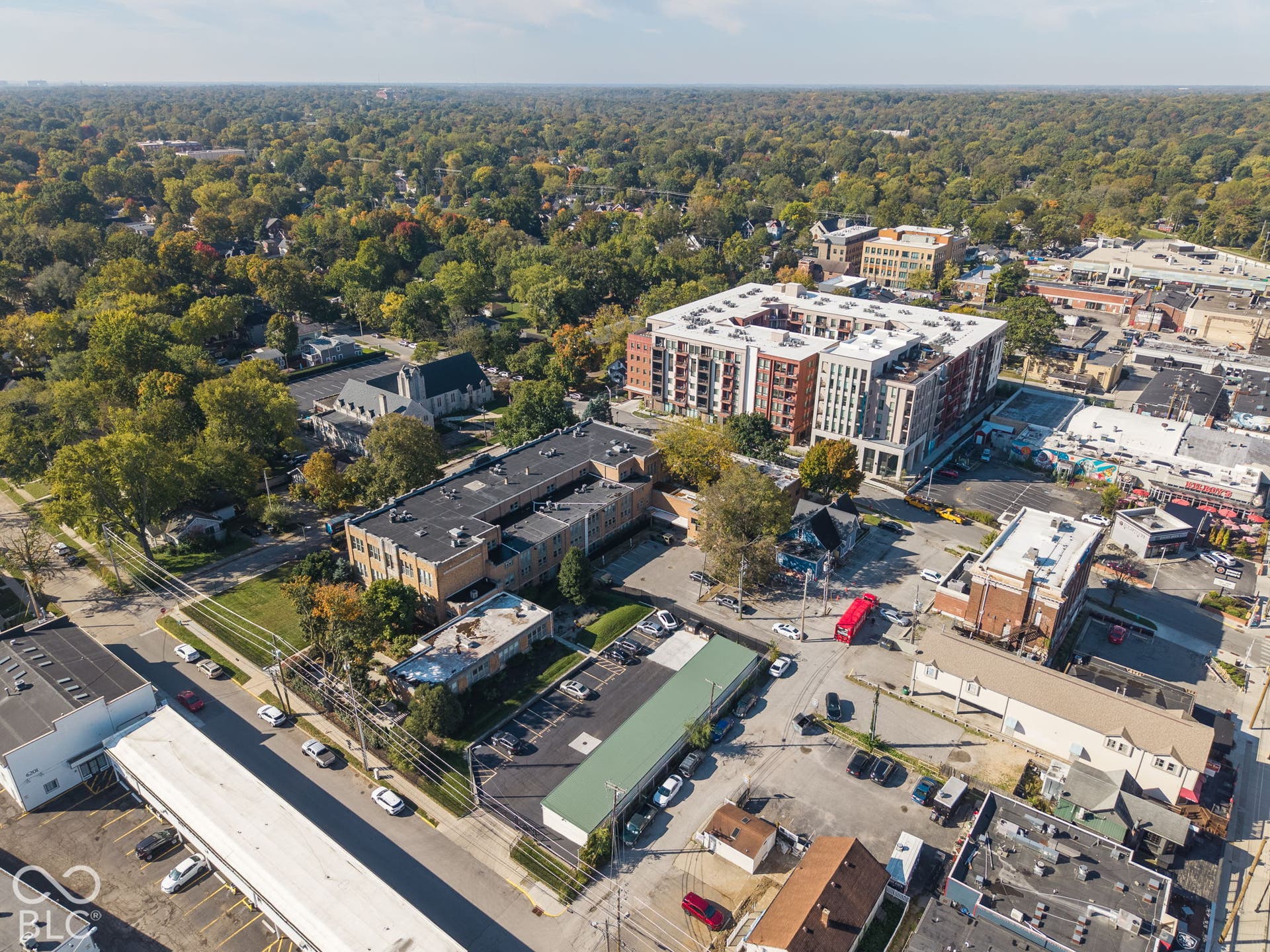 Aerial perspective of an urban center featuring paved surface parking, multi-level masonry structures, and proximity to dense mature tree canopy