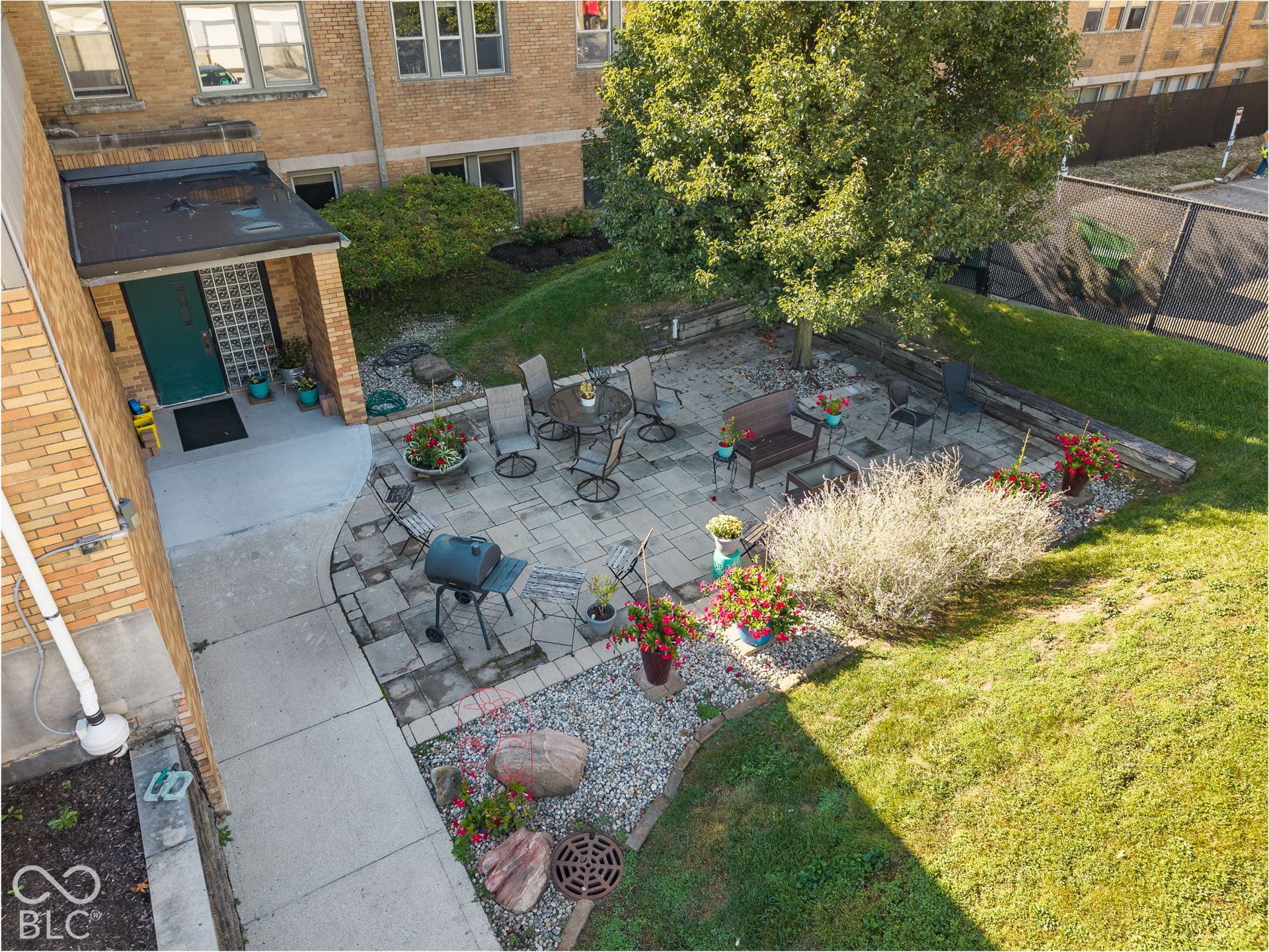 Paver patio featuring a concrete walkway, terraced landscaping with retaining walls, and mature shade trees