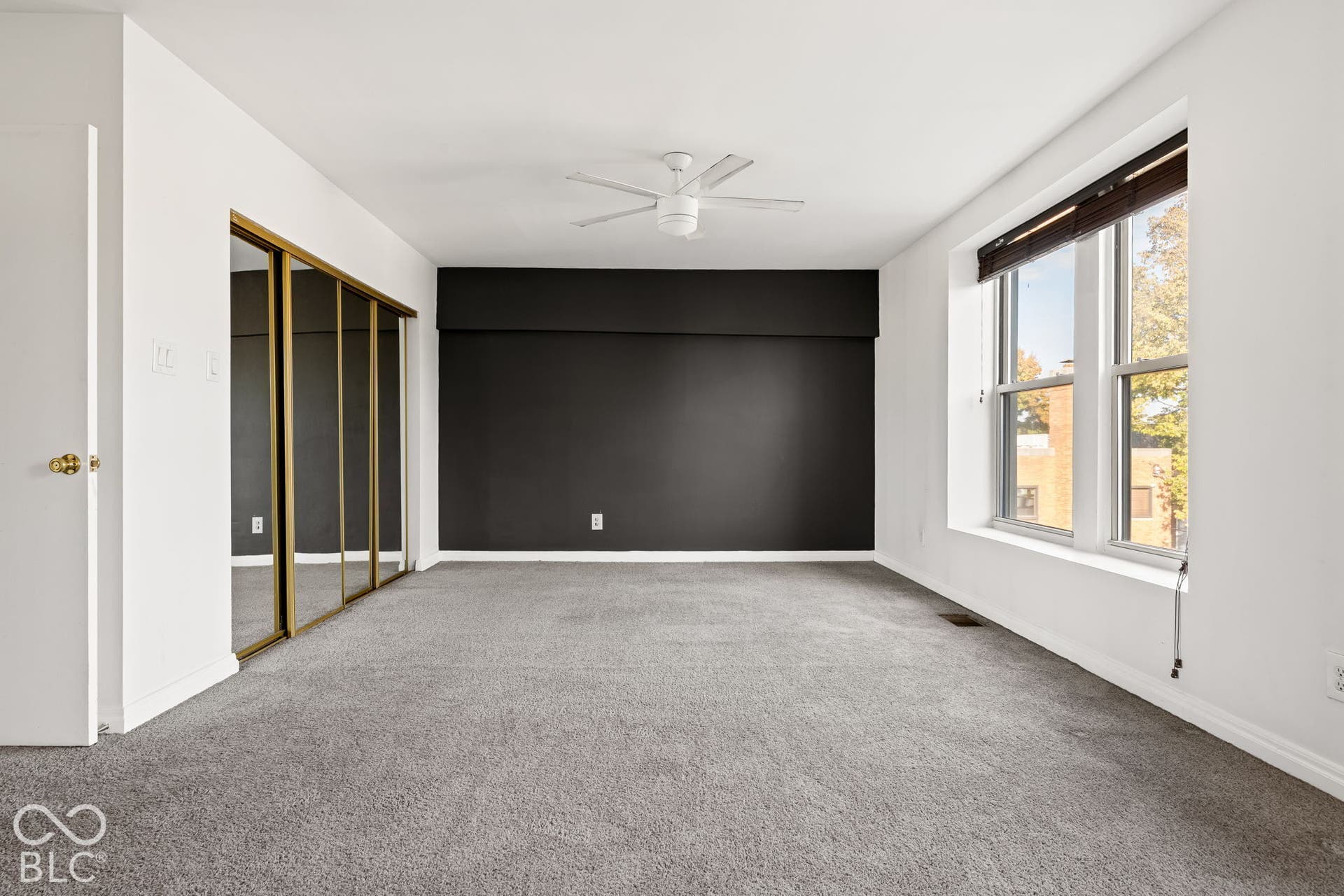 Interior space featuring wall-to-wall carpeting, floor-to-ceiling mirrored closet doors, a centered ceiling fan, and large windows with integrated blinds