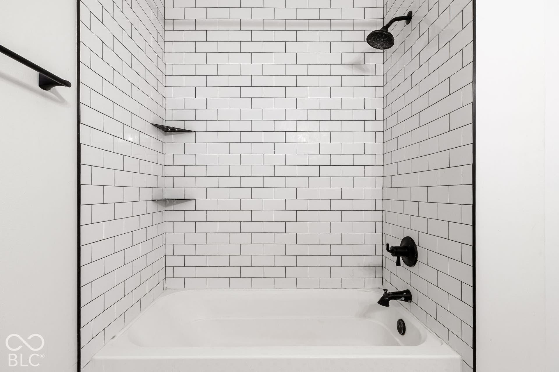 Bathtub with white subway tile surround, integrated corner shelving, and matte black fixtures