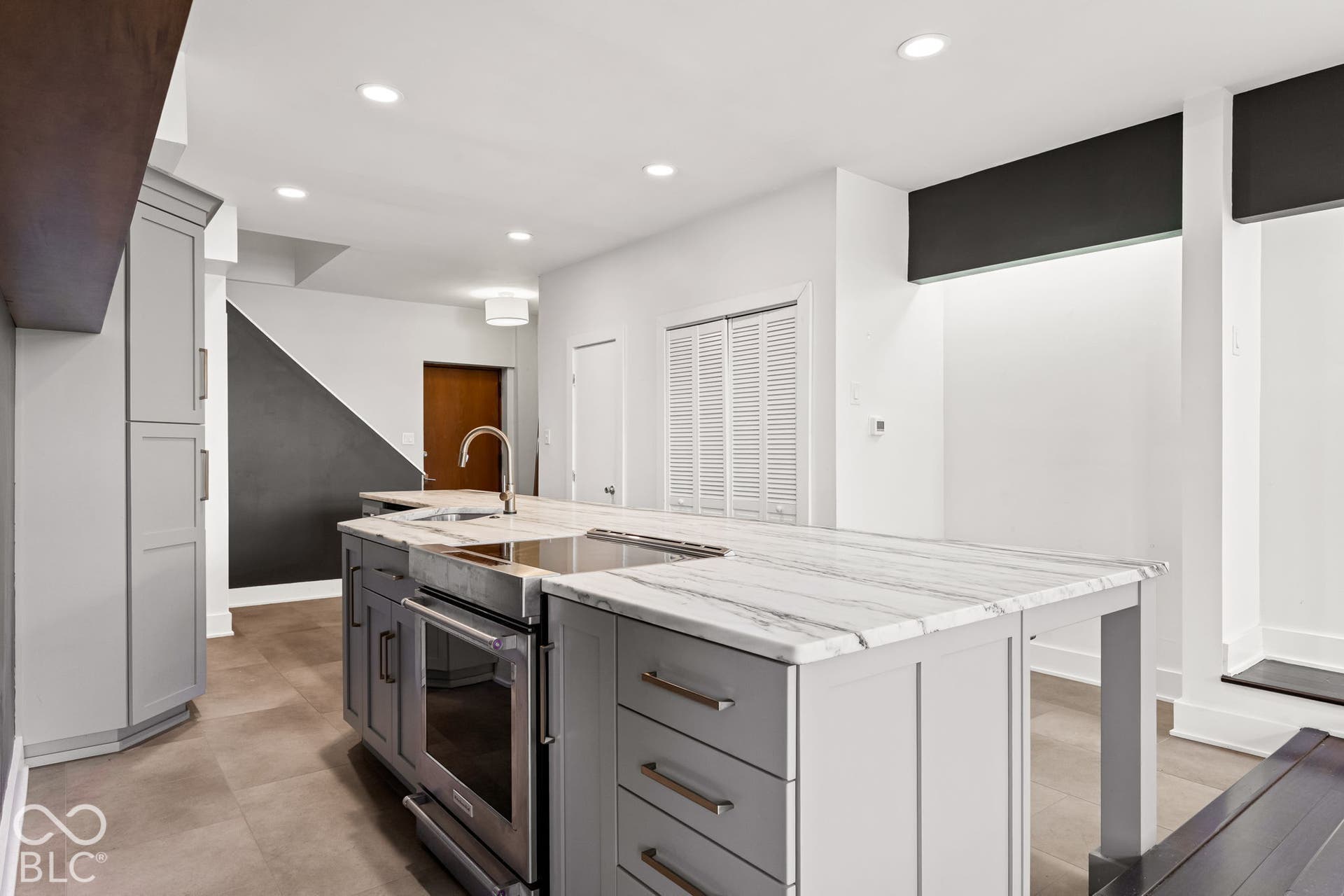Kitchen featuring a center island with light-toned stone countertops, built-in stainless steel oven and cooktop, gray shaker-style cabinetry, and recessed lighting