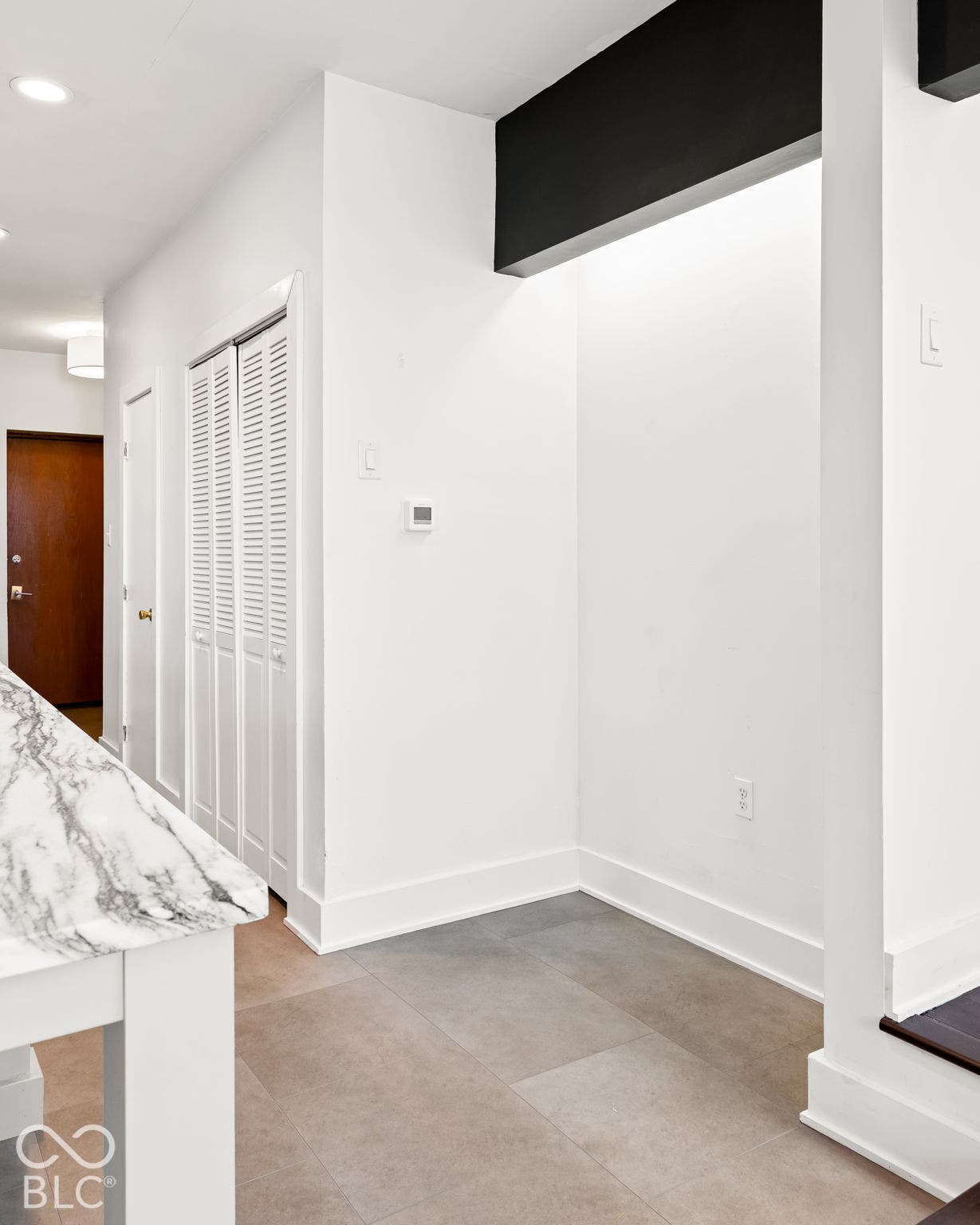 Interior space featuring neutral stone-finish tile flooring, white bi-fold closet doors, a high-contrast black accent beam, and a solid wood door