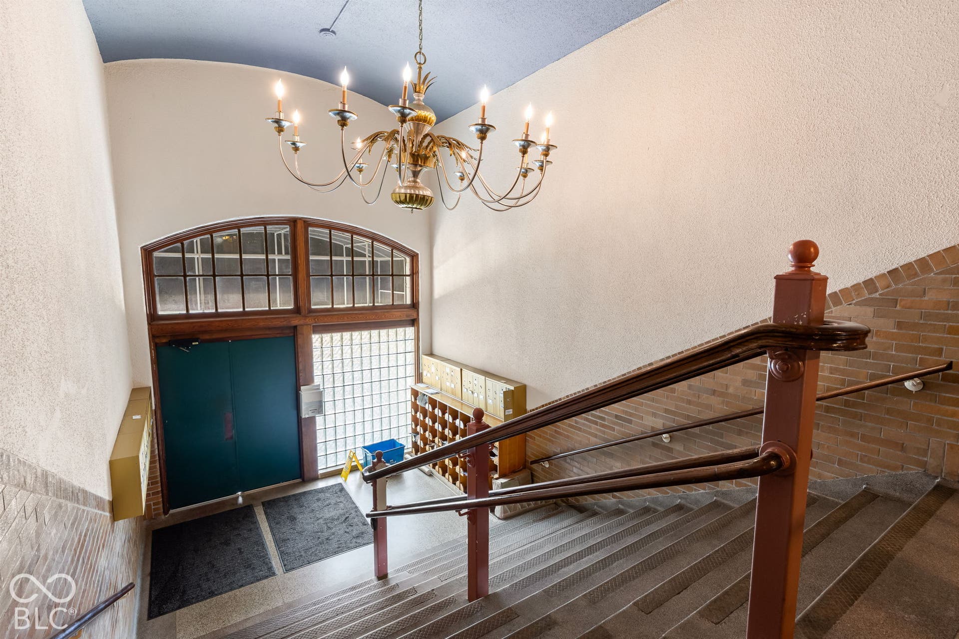 Entry featuring a vaulted ceiling with a multi-arm chandelier, arched multi-pane window, decorative glass block wall, and brick wall accents with a wood handrail