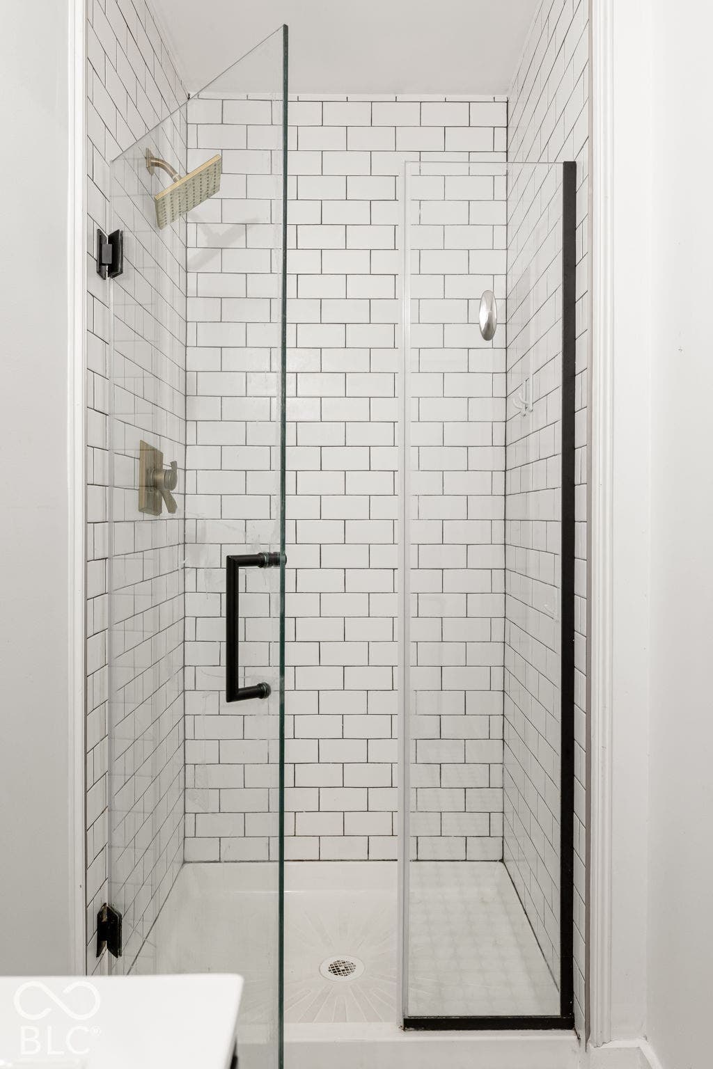 Walk-in shower featuring subway tile surround, frameless glass door, matte black hardware, and metallic finish showerhead