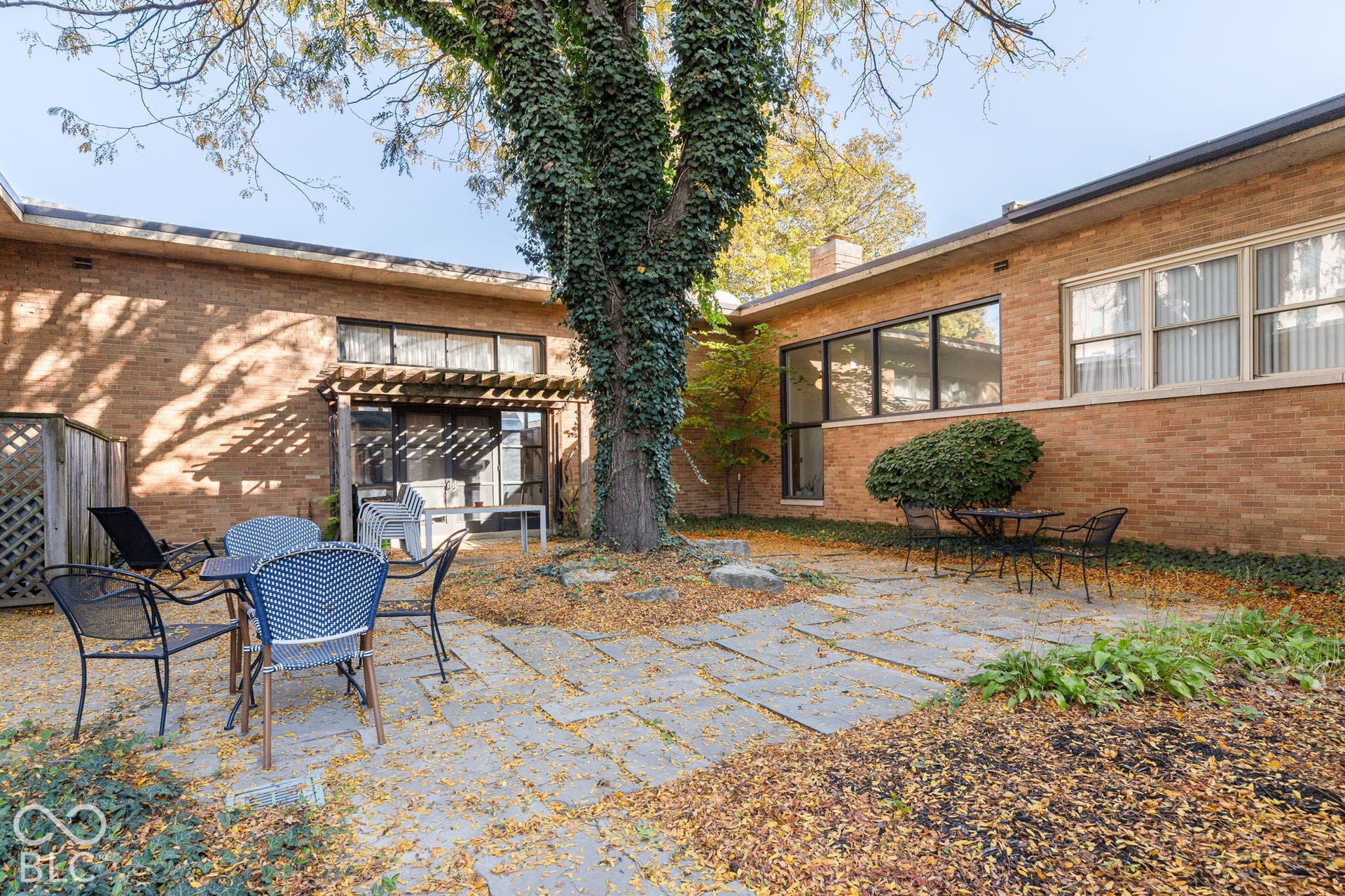 Flagstone patio featuring a central mature tree, exterior brick masonry, and a wooden pergola