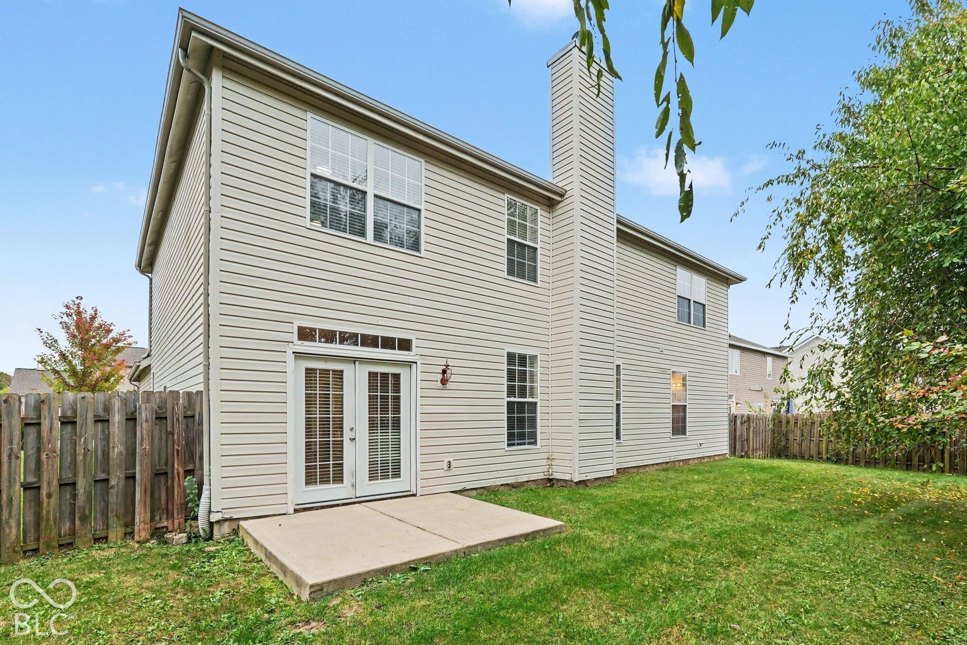 Rear exterior featuring horizontal vinyl siding, a concrete patio, exterior chimney, and double glass-pane doors
