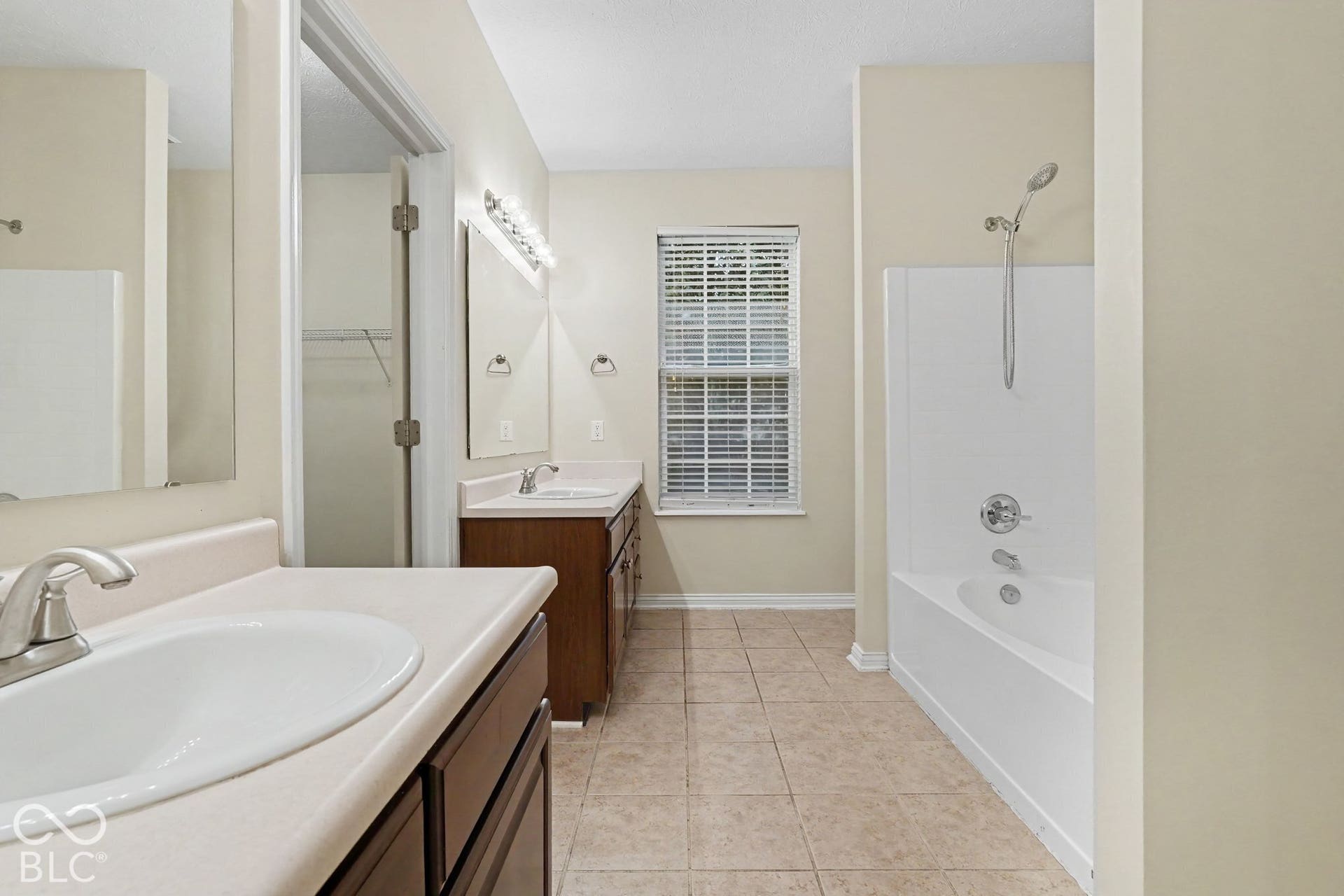 Bathroom featuring dual-sink wood cabinetry, solid-surface countertops, tile flooring, and a combined tub and shower surround