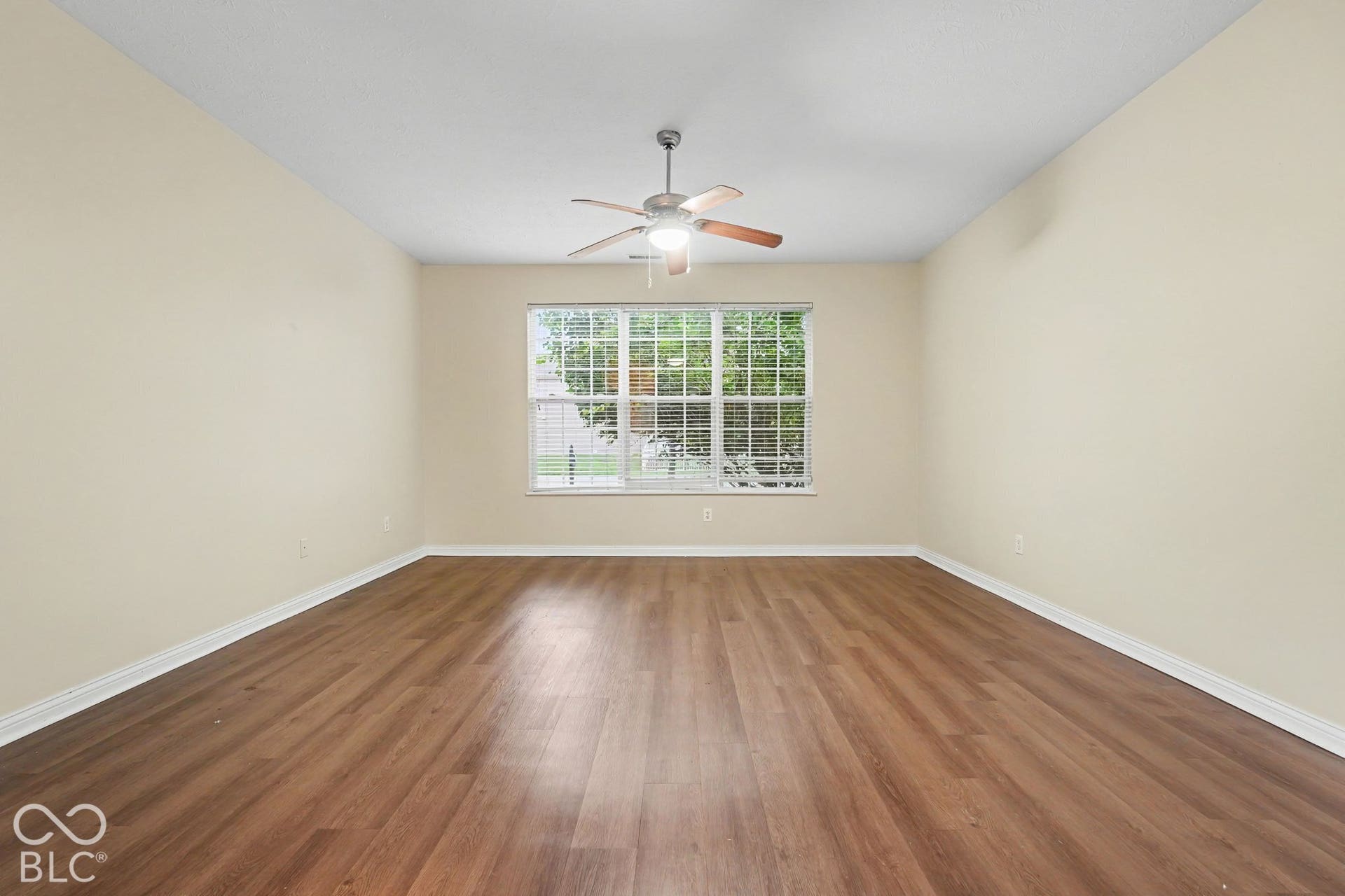 Neutral-toned interior room featuring wood-finish flooring, a multi-pane window, and a central ceiling fan with an integrated light fixture