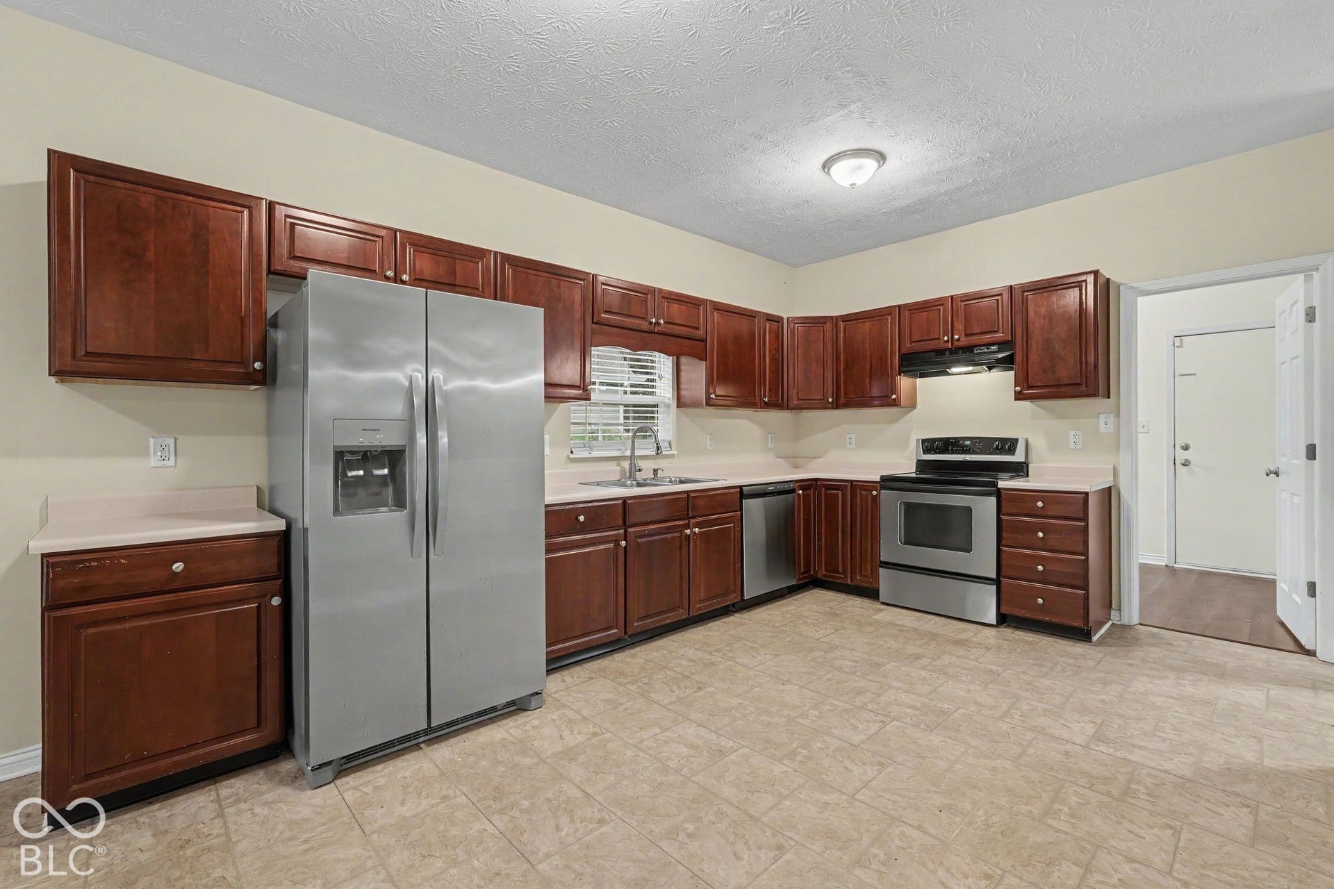 Kitchen featuring warm-tone wood cabinetry, solid-surface countertops, stainless steel appliances, and tile flooring