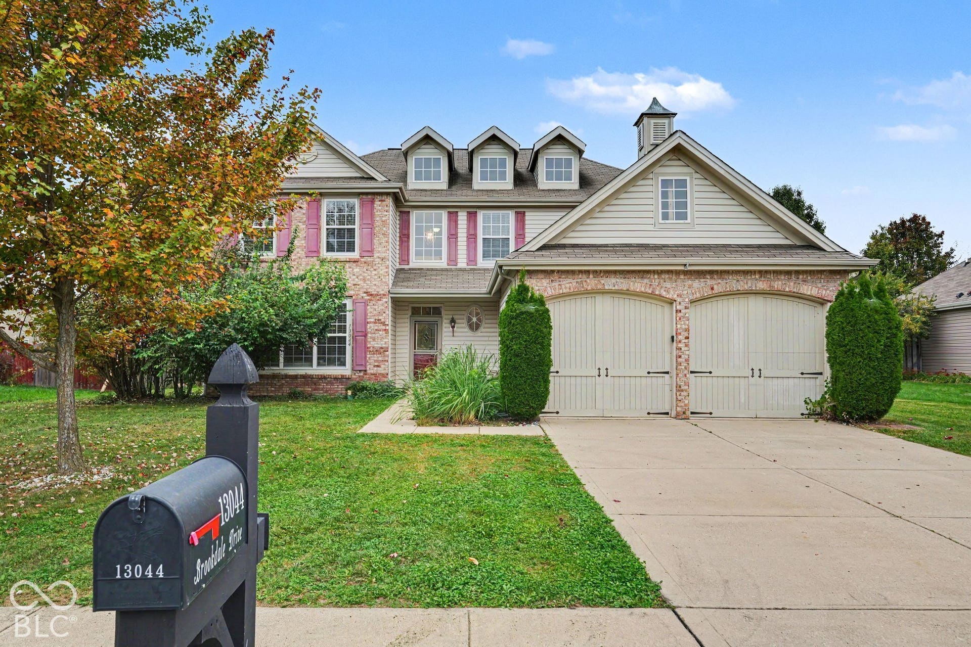 Two-story residence with brick and horizontal siding exterior, featuring three roof dormers, a cupola, and a dual-bay garage with carriage-style doors