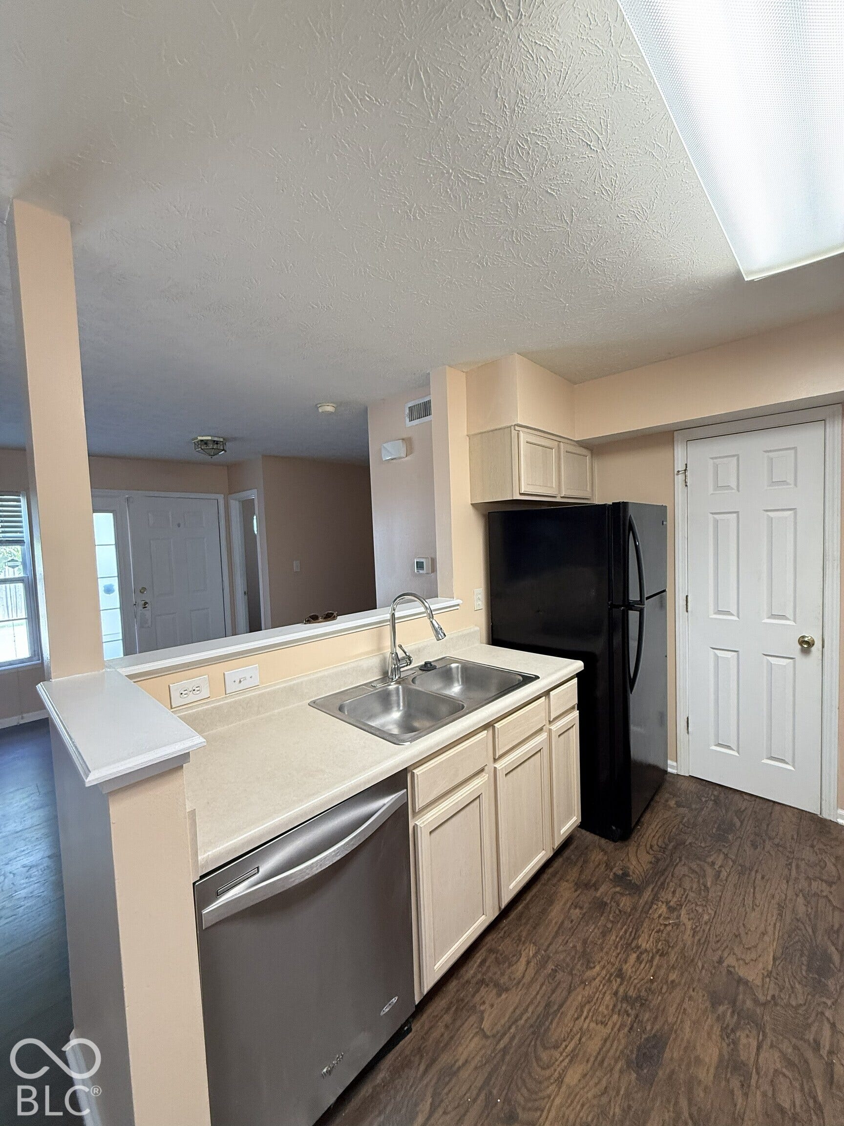 Kitchen featuring wood-finish flooring, light-toned cabinetry, dual-basin stainless steel sink with high-arc faucet, and black refrigerator