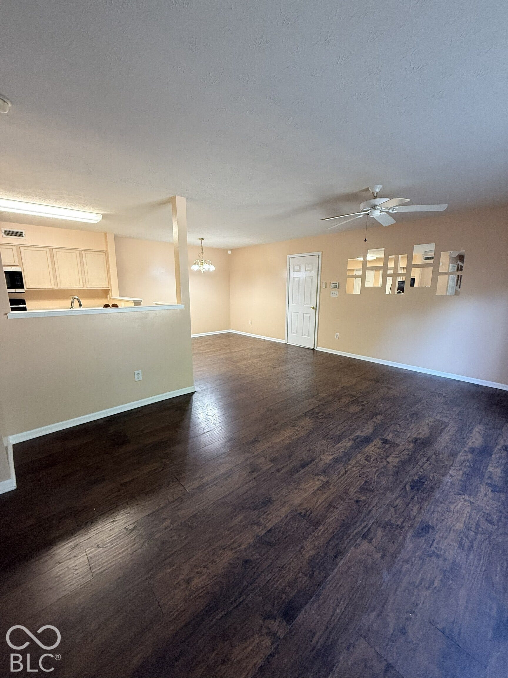 Open-concept living space featuring wood-finish flooring, white cabinetry, integrated ceiling fan, and geometric wall-mounted mirrors
