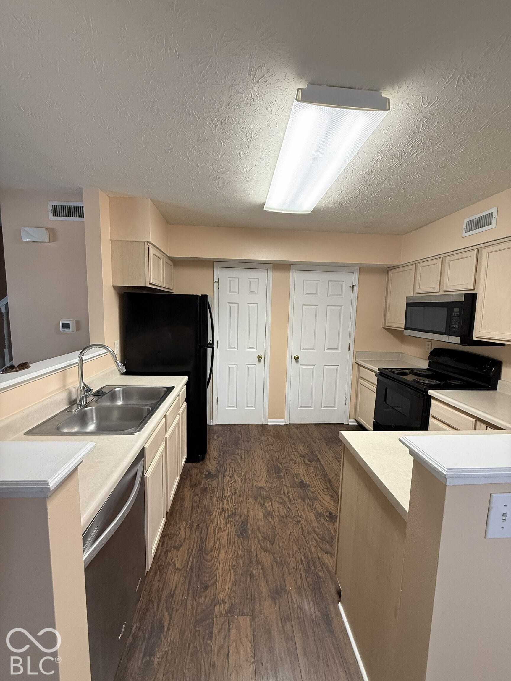 Kitchen featuring wood-finish flooring, light-toned cabinetry, dual-basin stainless steel sink, over-the-range microwave, and two interior doors