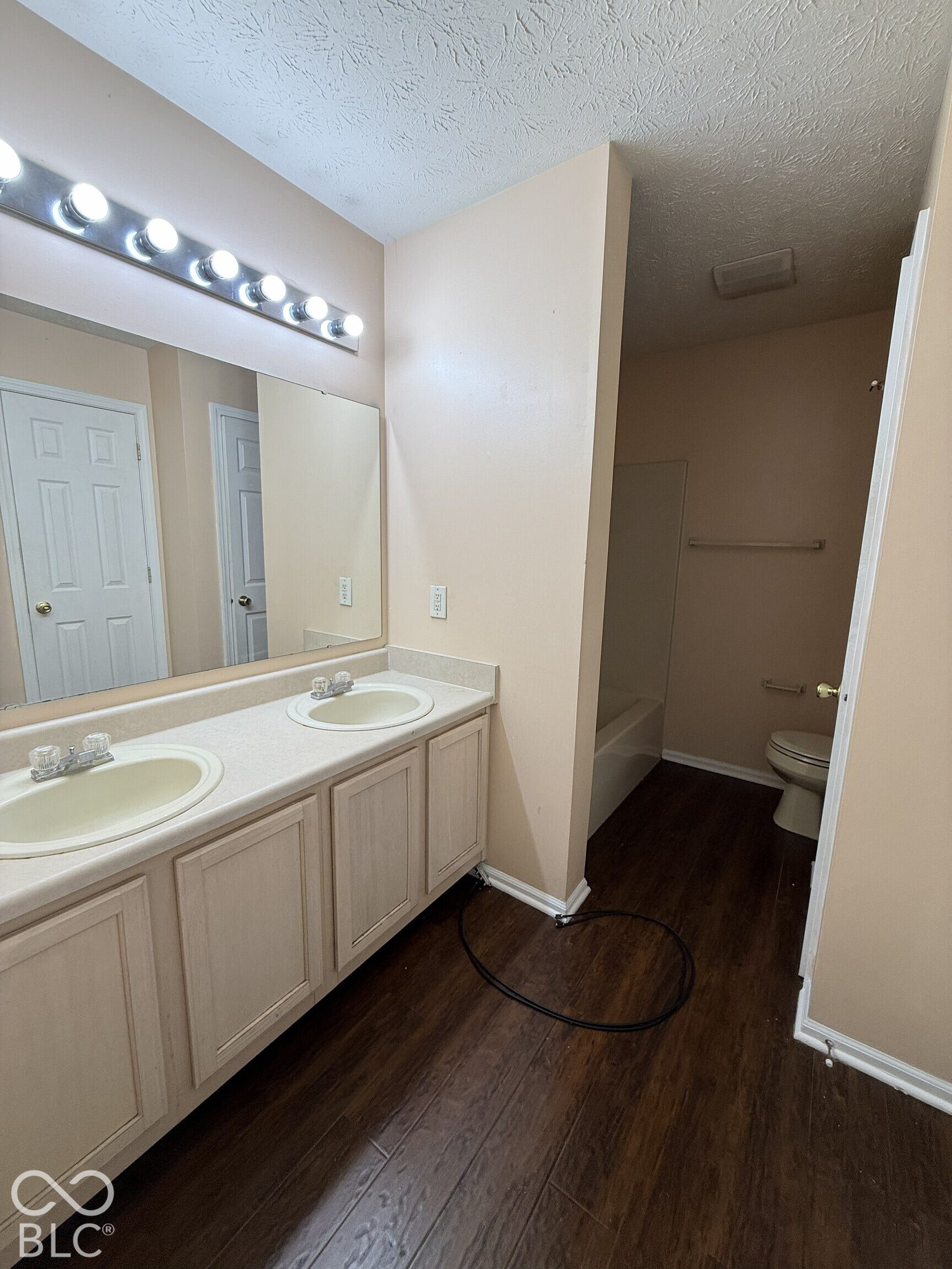 Double vanity featuring light-toned cabinetry, dual drop-in sinks, a solid-surface countertop, and wood-finish flooring