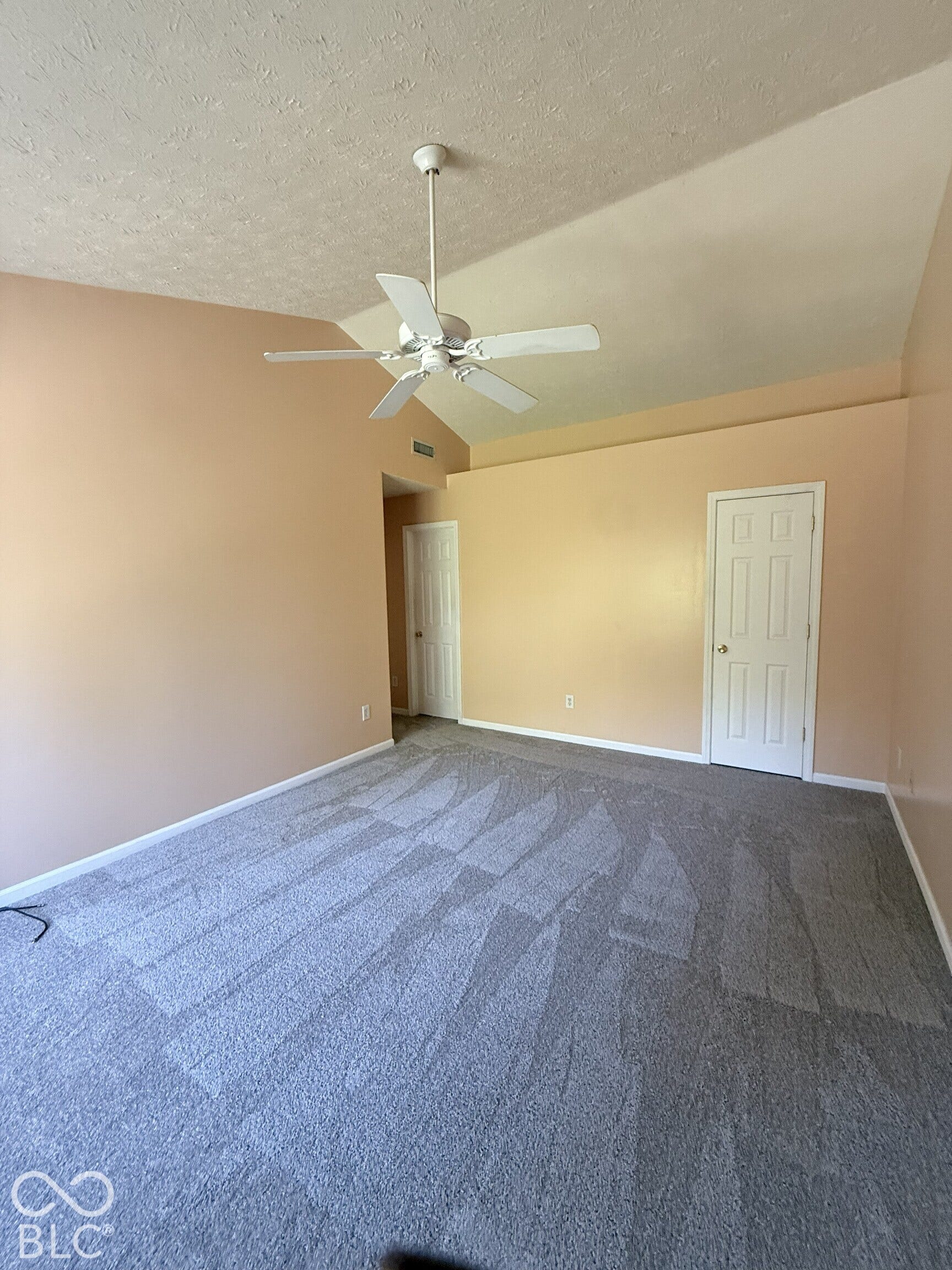 Vaulted ceilings featuring a white central ceiling fan, neutral wall tones, and neutral-toned wall-to-wall carpeting