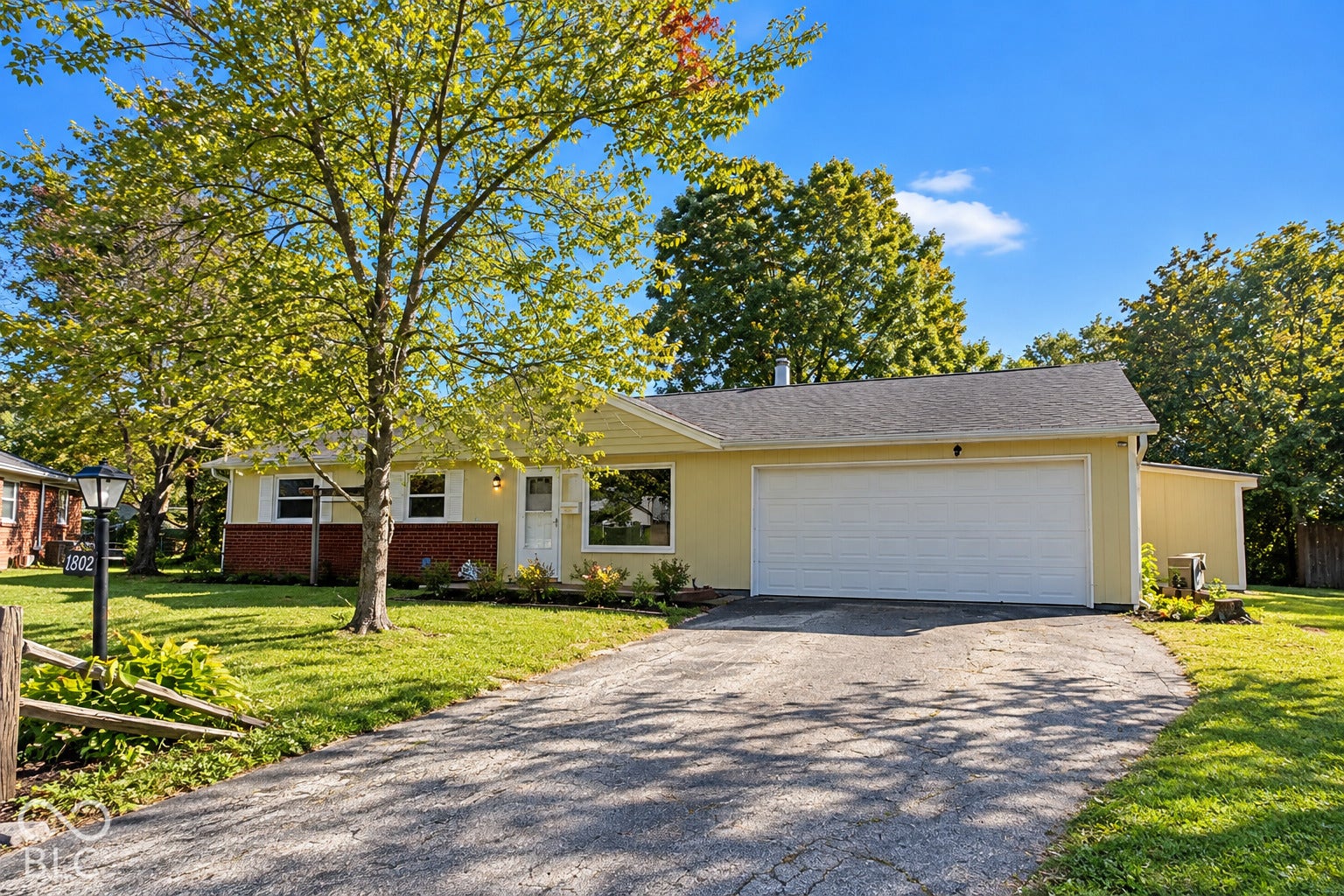 1802 Heather Court, Indianapolis, IN 46229 Virtually Altered - Ranch-style exterior featuring horizontal siding, a red brick veneer facade, attached two-car garage, asphalt driveway, and mature landscaping