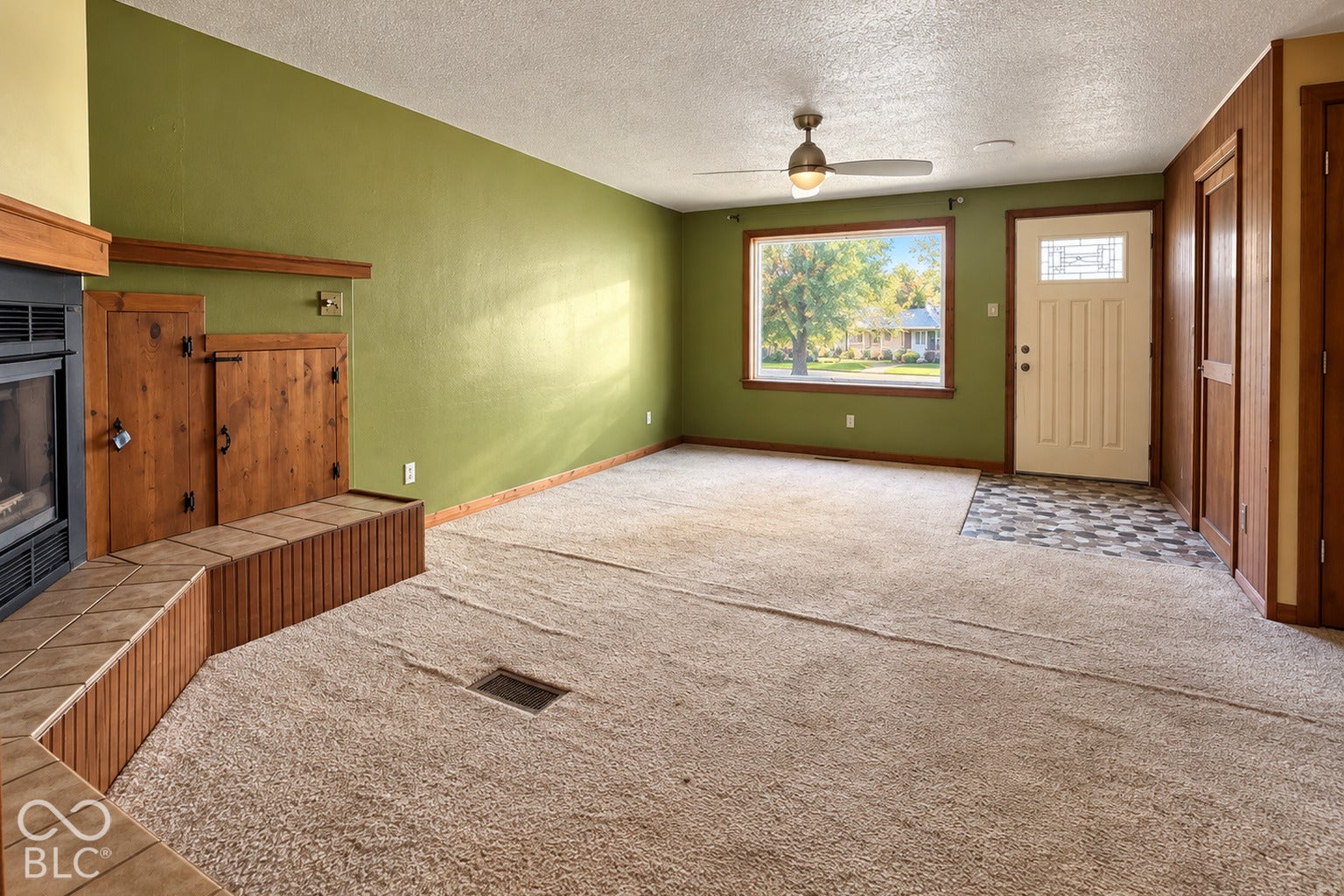 1802 Heather Court, Indianapolis, IN 46229 Virtually Altered - Fireplace with tile hearth and wood surround, neutral carpeting, ceiling fan, large window, and paneled front door with sidelight inlay