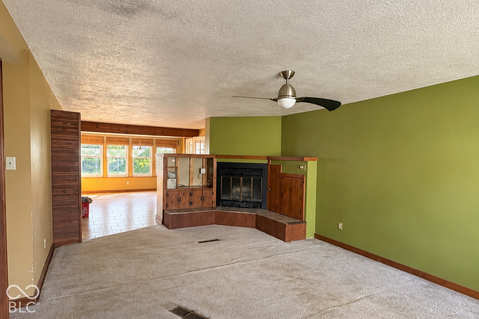 1802 Heather Court, Indianapolis, IN 46229 Virtually Altered - Corner fireplace with wood-paneled surround, integrated cabinetry, brushed nickel ceiling fan with light kit, and natural light exposure