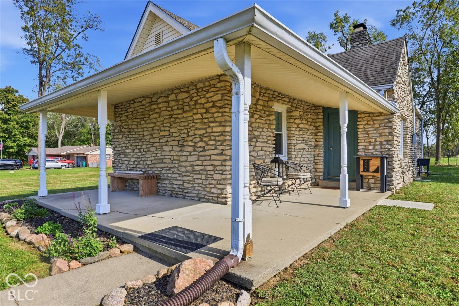 Exterior facade featuring natural stone masonry, a covered porch with slender structural columns, a concrete patio, and a stone chimney