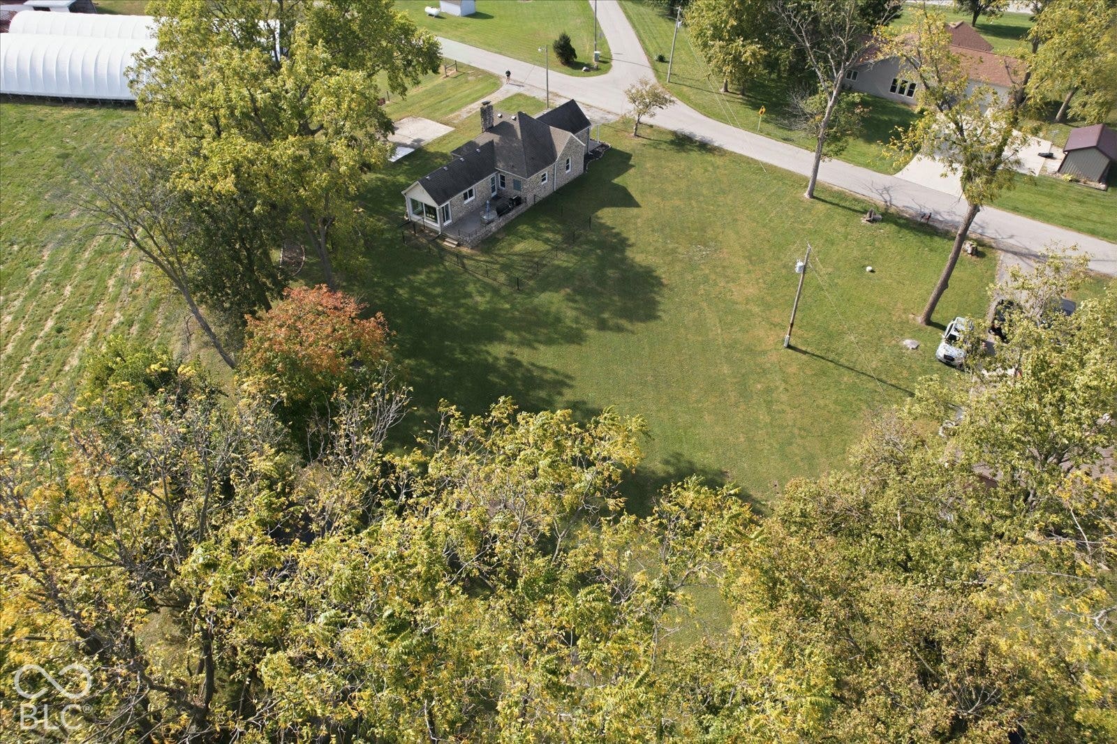 Aerial view of a sprawling property featuring a multi-gabled residence, an expansive grassy lawn, mature trees, and a wooden deck