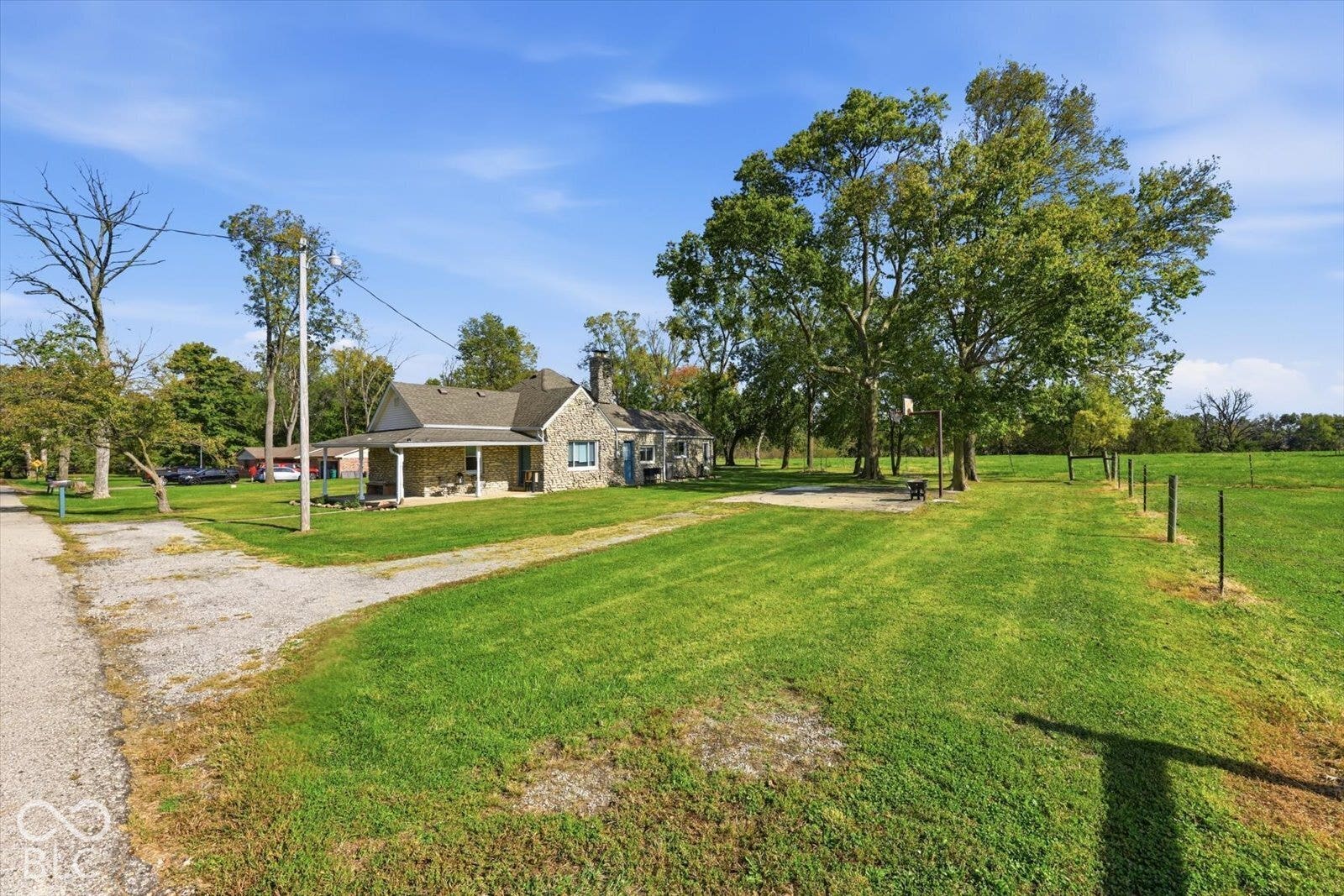 Stone-veneer exterior featuring a covered front porch, exterior stone chimney, gravel driveway, and mature trees on a spacious lot