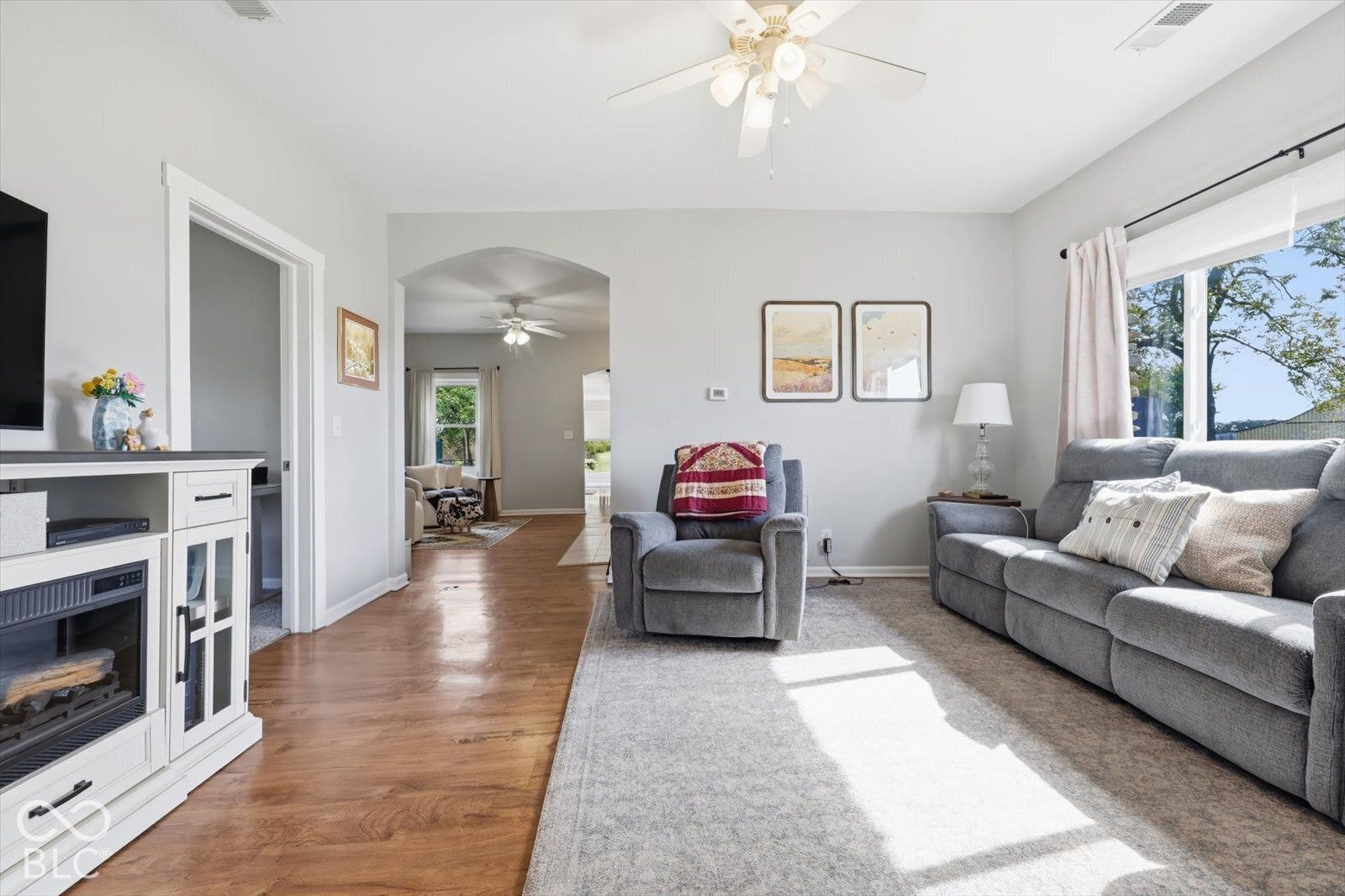 Living area featuring wood-finish flooring, a ceiling fan with integrated lighting, and an arched entryway