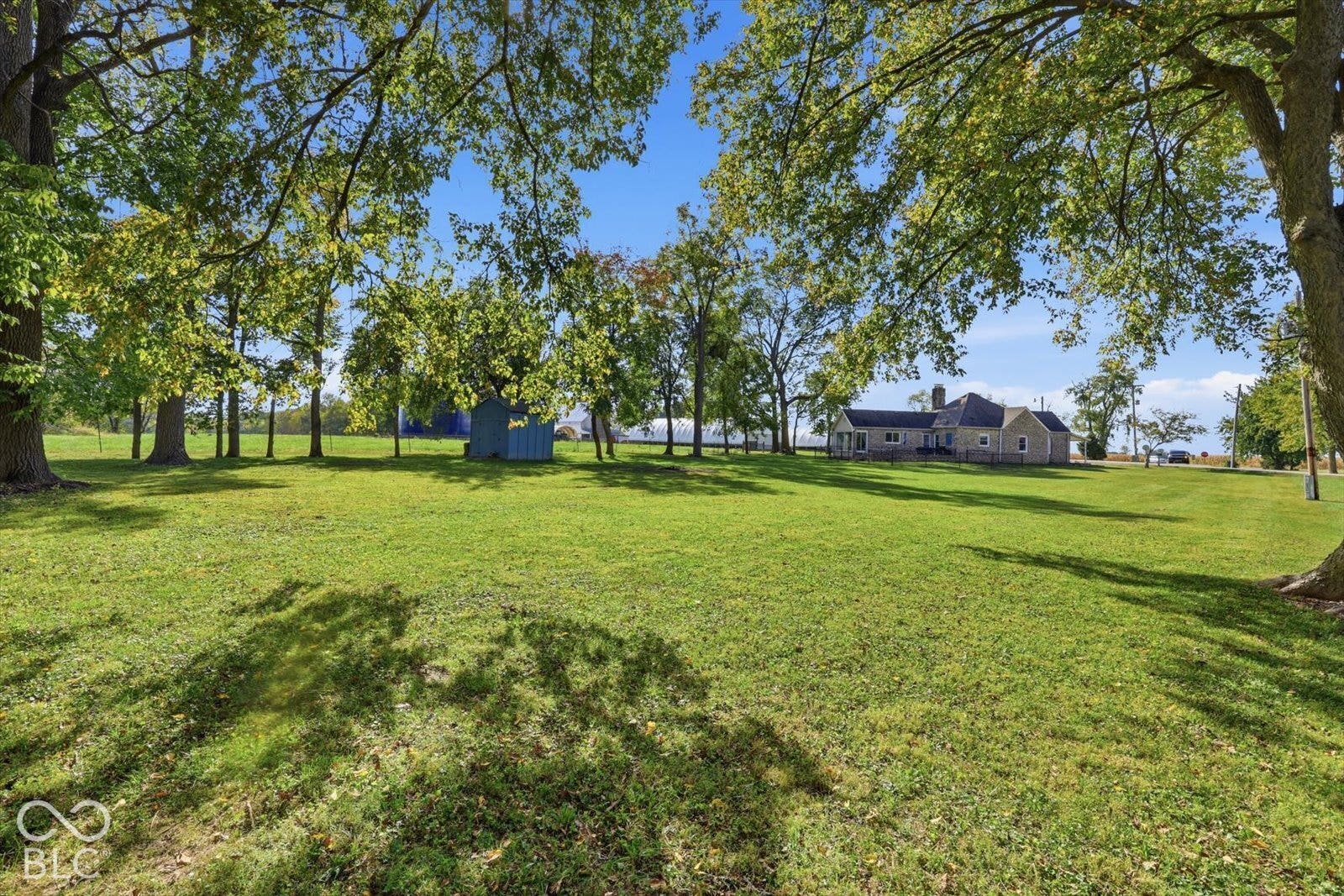 Expansive grounds featuring mature shade trees, a grass lawn, and an exterior storage structure