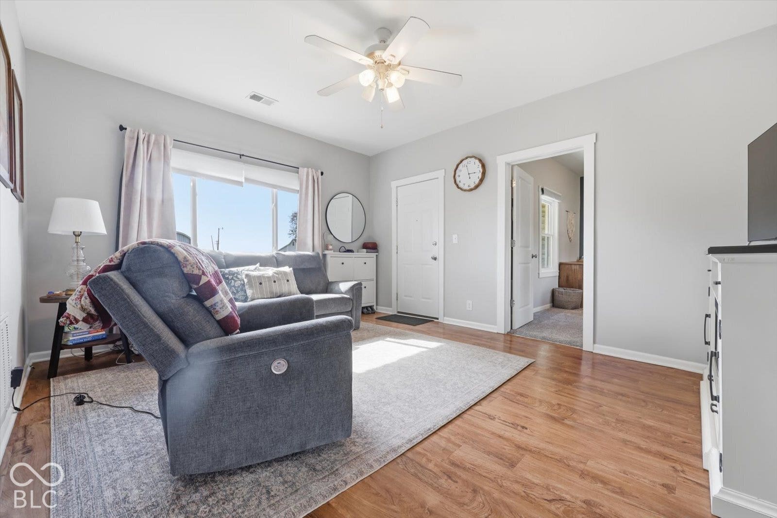 Living area featuring wood-finish flooring, a multi-blade ceiling fan with integrated lighting, and neutral wall paint
