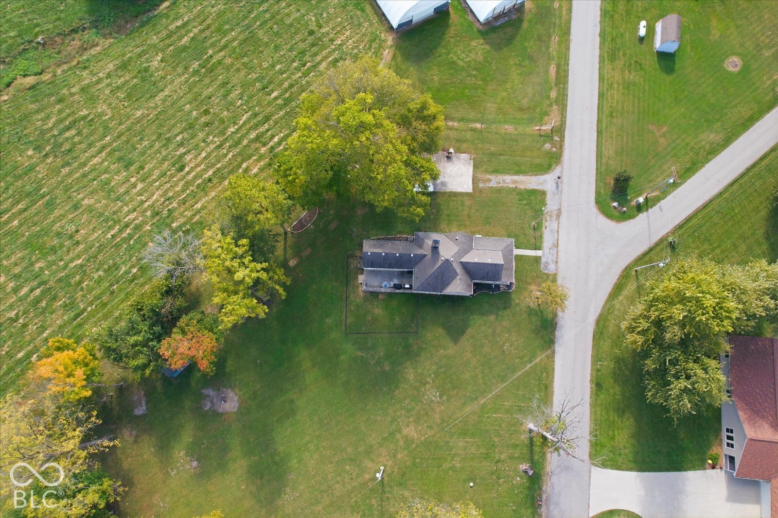 Aerial perspective featuring a multi-gabled roofline, expansive grass acreage, mature tree canopy, and paved driveway access