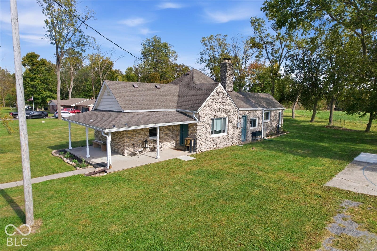 Stone exterior residence featuring a covered front porch, a prominent stone chimney, and expansive surrounding grounds
