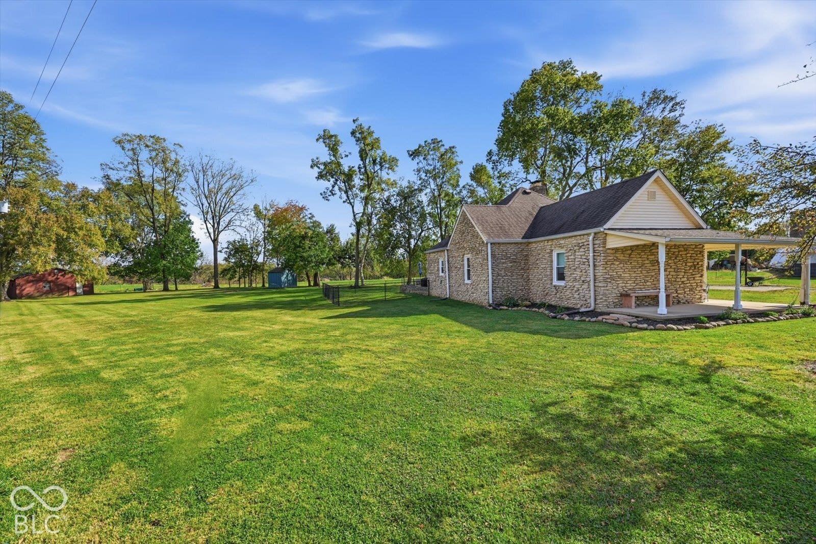 Expansive yard featuring stone-exterior siding, a covered porch, mature trees, and an additional detached storage structure