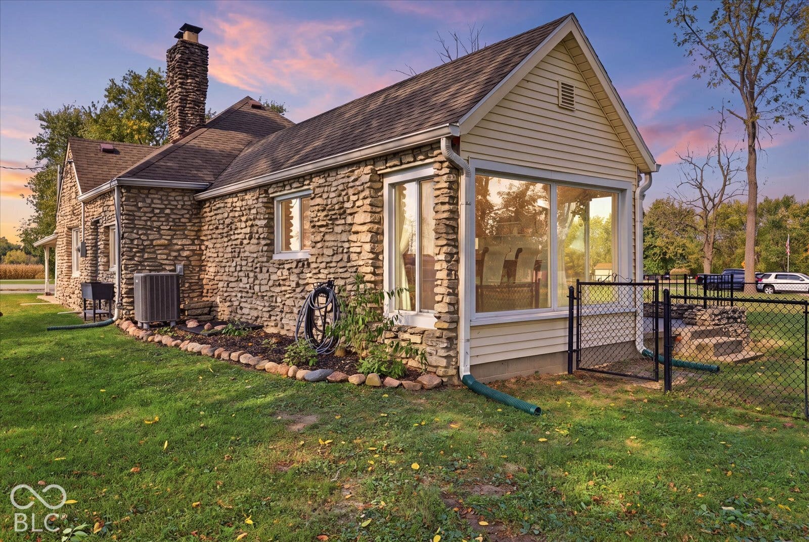 Virtually Altered - Exterior featuring natural stone masonry, horizontal siding, an oversized chimney, large picture windows, and a fenced yard