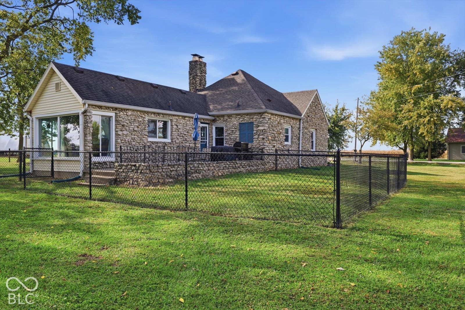 Exterior featuring stone masonry siding, an attached stone chimney, a paved patio area, and a fenced-in yard