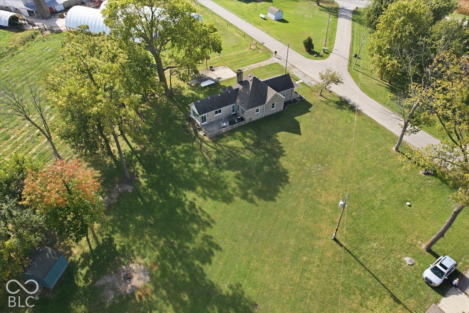 Aerial perspective of a detached residence featuring a stone exterior, a paved patio, and mature trees situated on a grass-covered lot