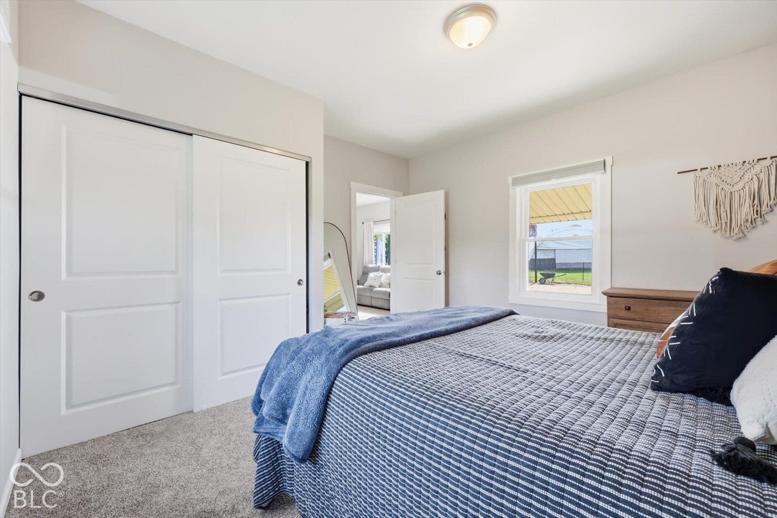 Neutral-toned bedroom featuring carpeting, double-door closet with paneled detailing, and a single-hung window with casing