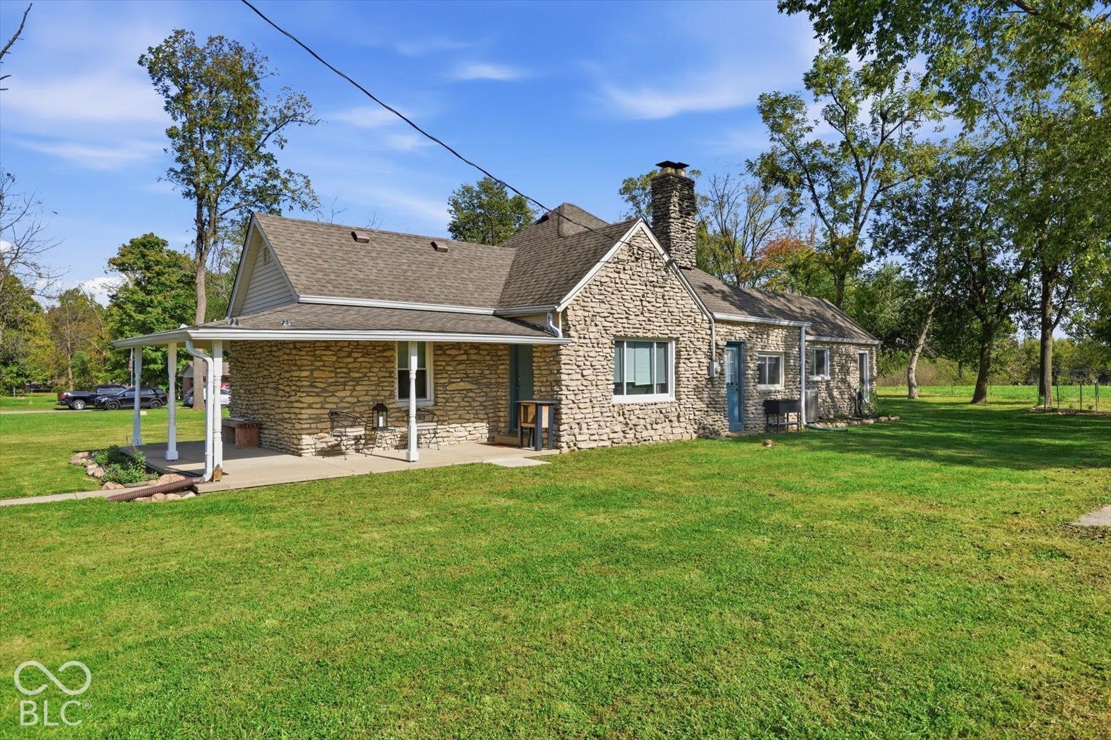 Stone exterior with a prominent stone chimney, shingled roof, and a covered patio on a spacious lot