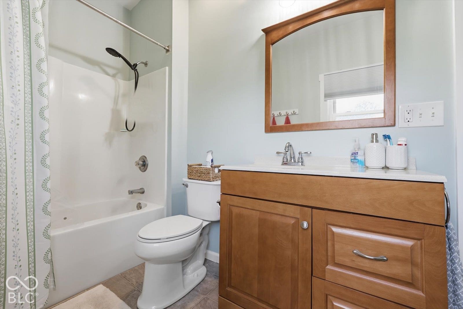 Bathroom featuring a wood-finish vanity with a stone-top integrated sink, a matching wooden-framed wall mirror, and a white acrylic soaking tub with a shower fixture