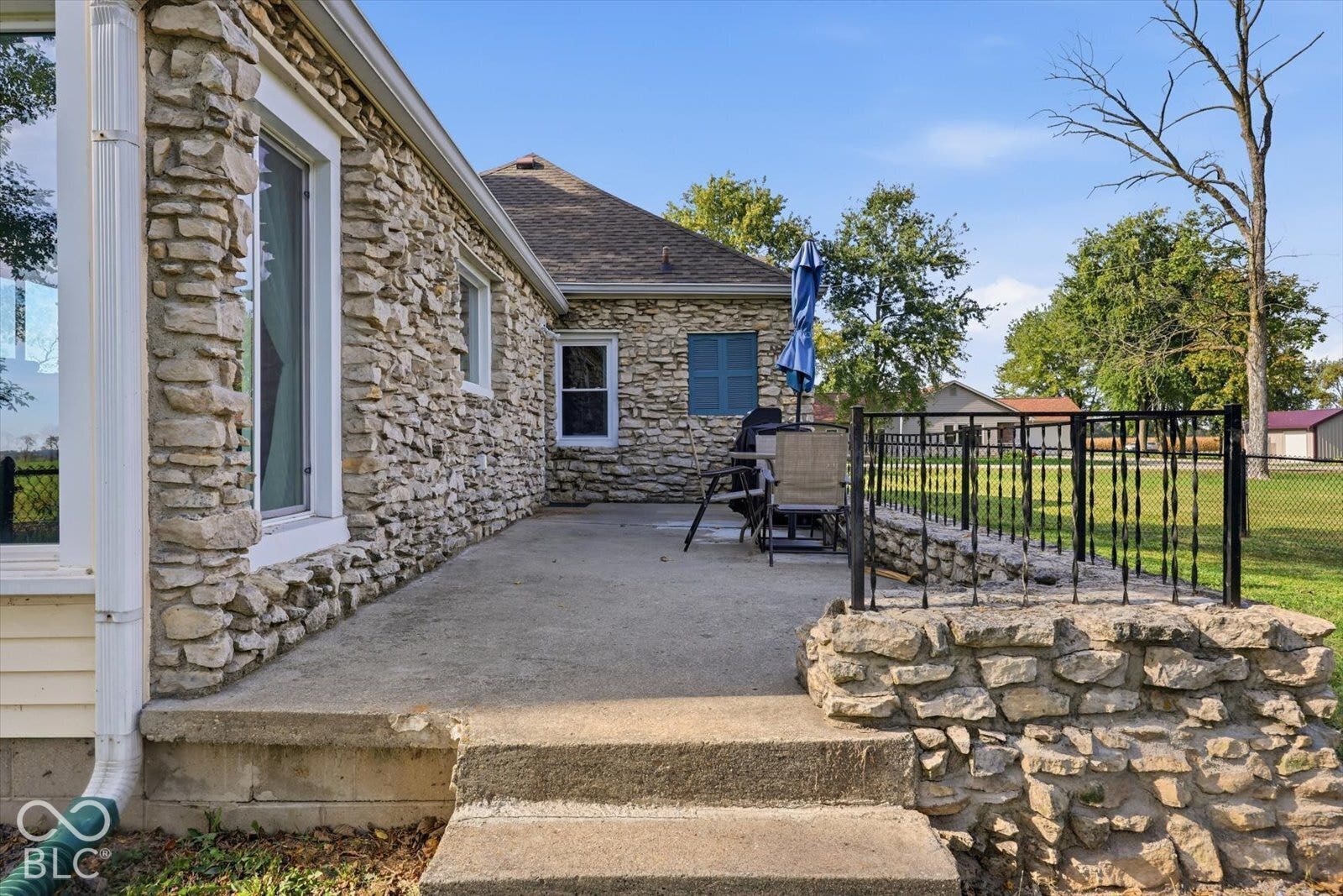 Exterior stone facade featuring a concrete patio, stone-accented perimeter wall, and black metal fencing