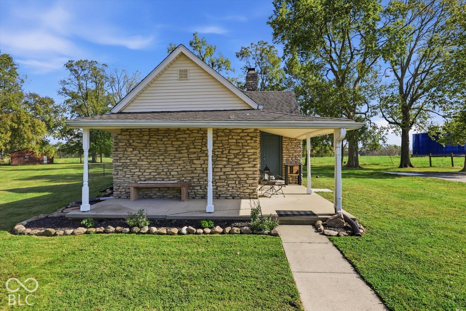 Exterior featuring stacked stone masonry, a covered porch with white support columns, concrete walkway, and expansive grassy grounds
