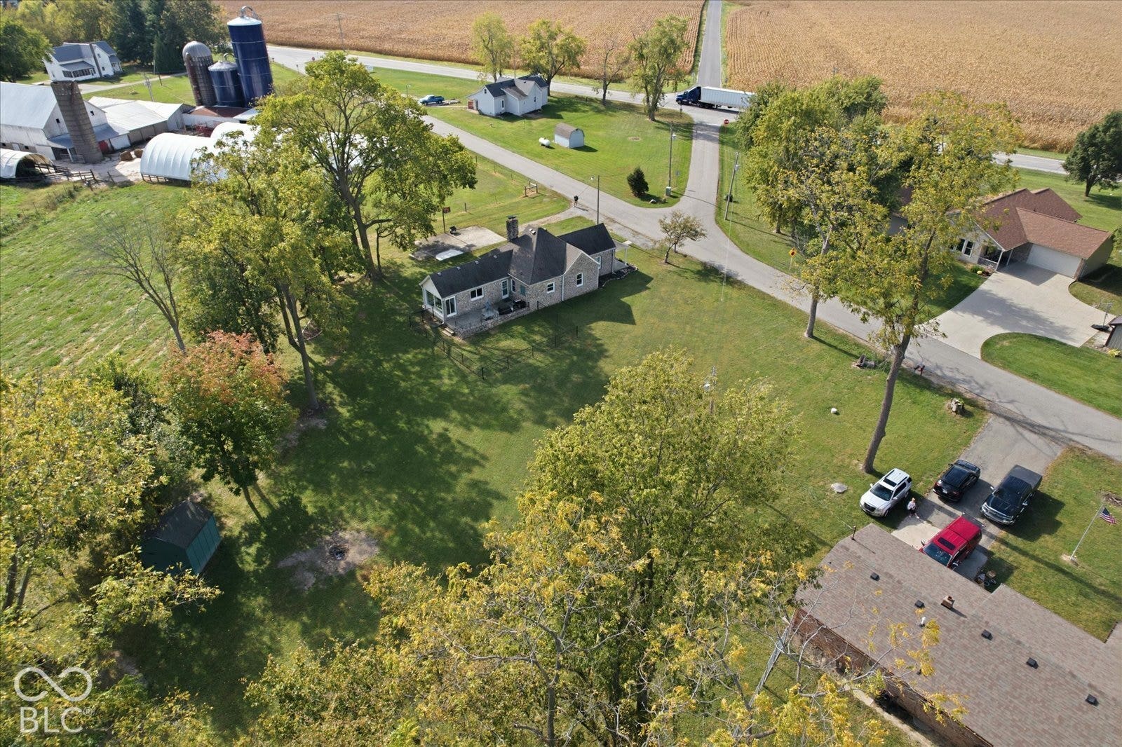 Aerial perspective of property featuring extensive open acreage, mature trees, concrete driveway, and structural outbuildings