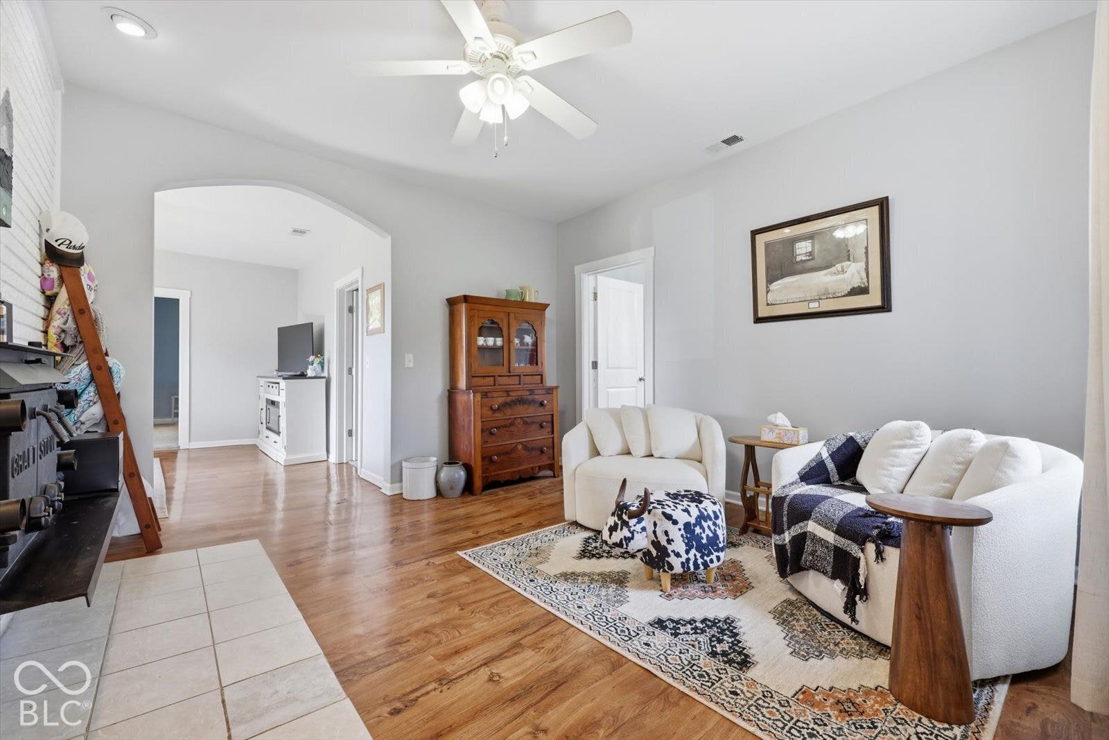 Living area featuring wood-finish flooring, a recessed fireplace with a tile hearth, a central ceiling fan with integrated lighting, and an arched entryway