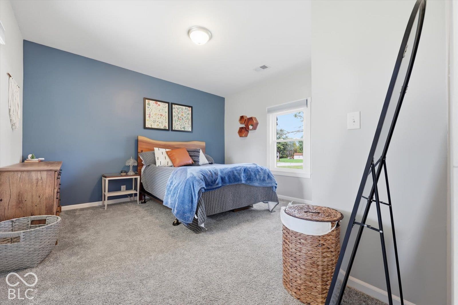 Neutral-toned carpeted flooring, striking blue accent wall, and natural light from the window